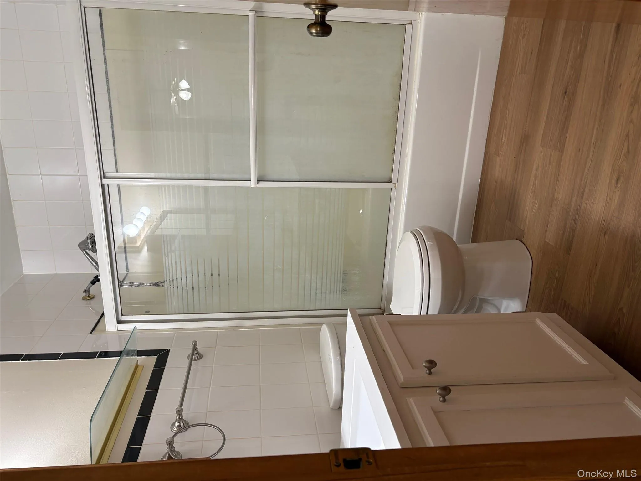 Bathroom featuring combined bath / shower with glass door, vanity, dark wood-style flooring, and tile walls Bathroom featuring combined bath / shower with glass door, vanity, dark wood-style flooring, and tile walls