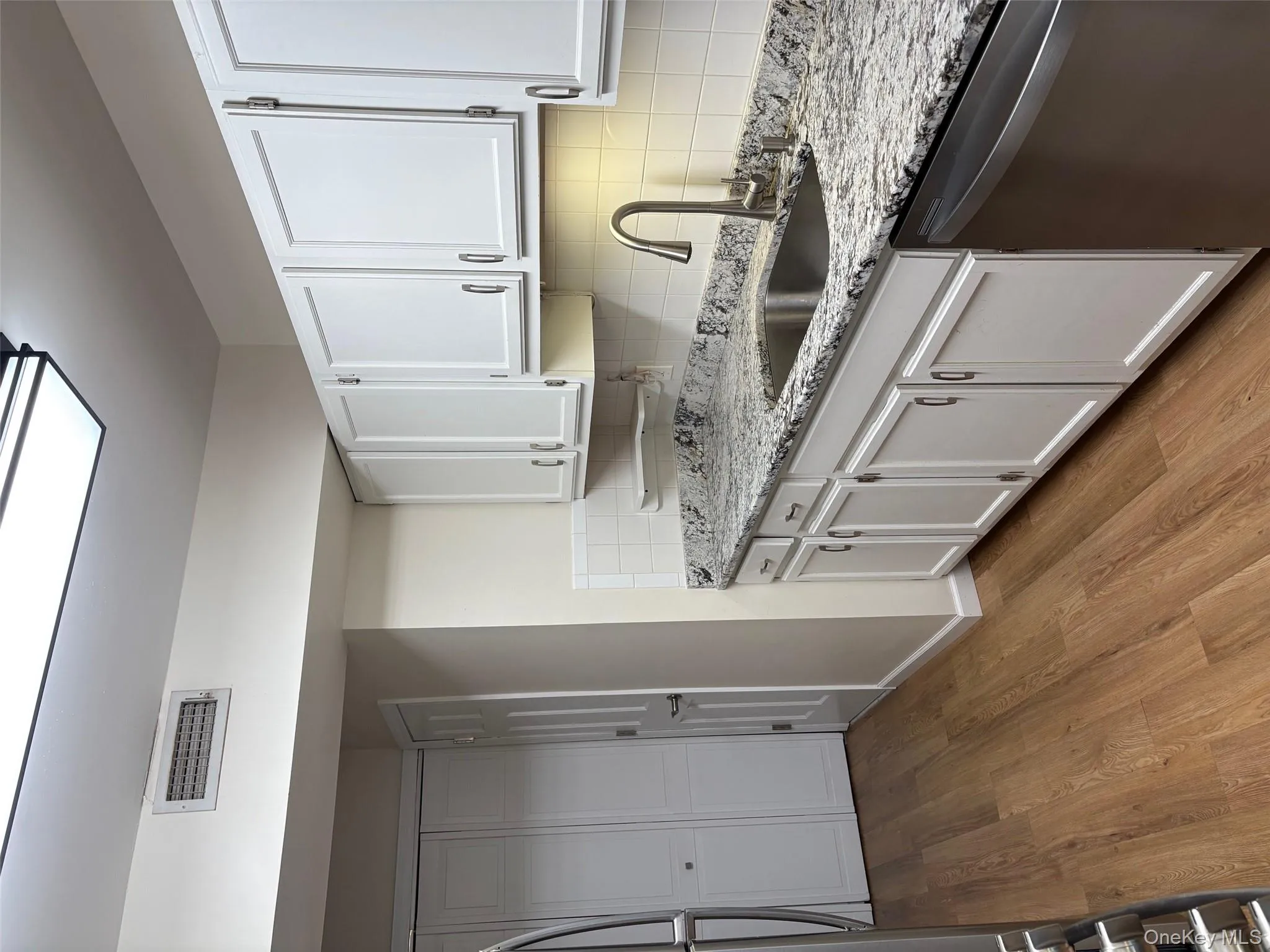 Kitchen with tasteful backsplash, dishwasher, white cabinetry, and light wood-type flooring Kitchen with tasteful backsplash, dishwasher, white cabinetry, and light wood-type flooring