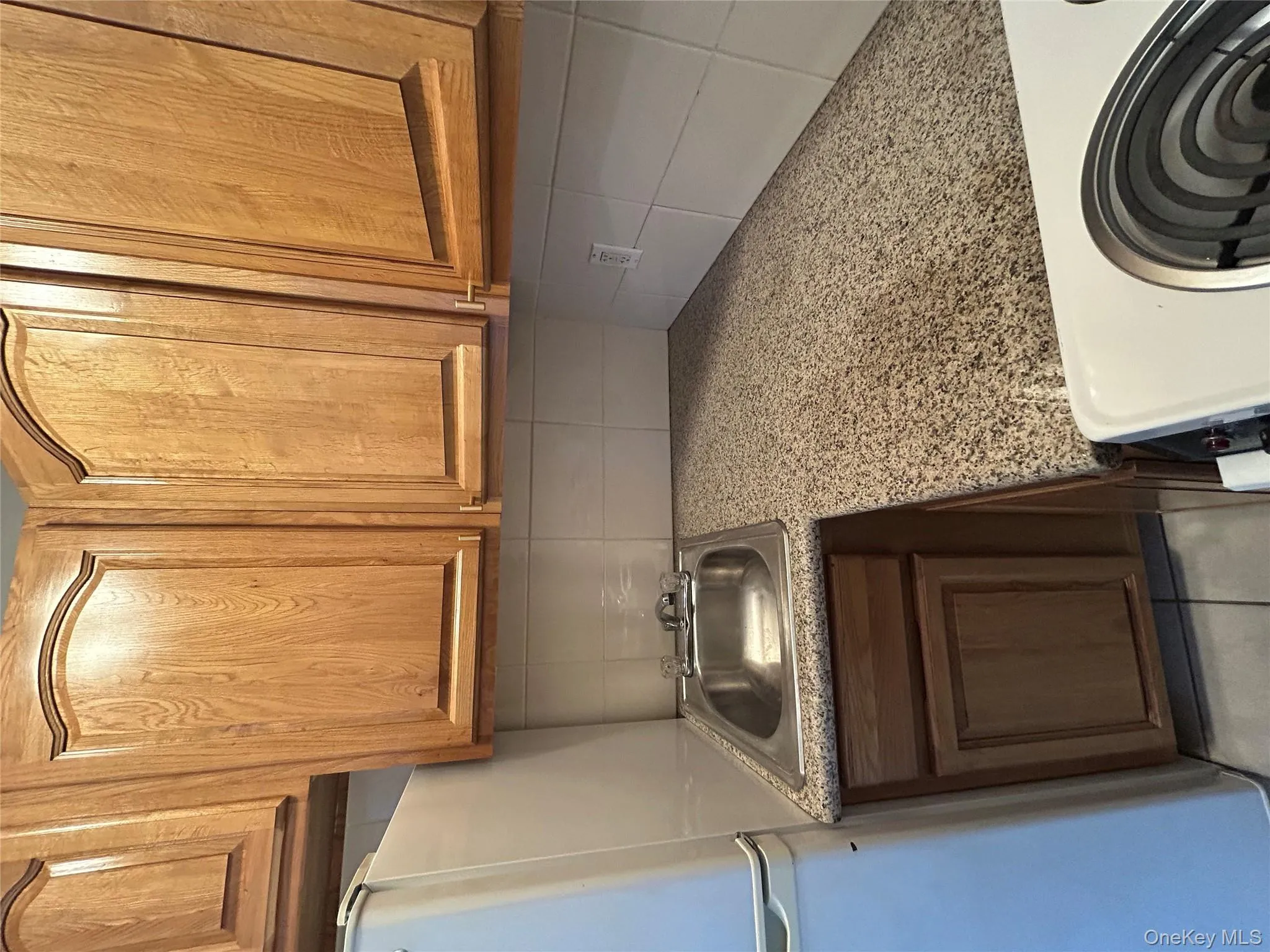 Kitchen with backsplash, paneled fridge, brown cabinetry, and white range Kitchen with backsplash, paneled fridge, brown cabinetry, and white range