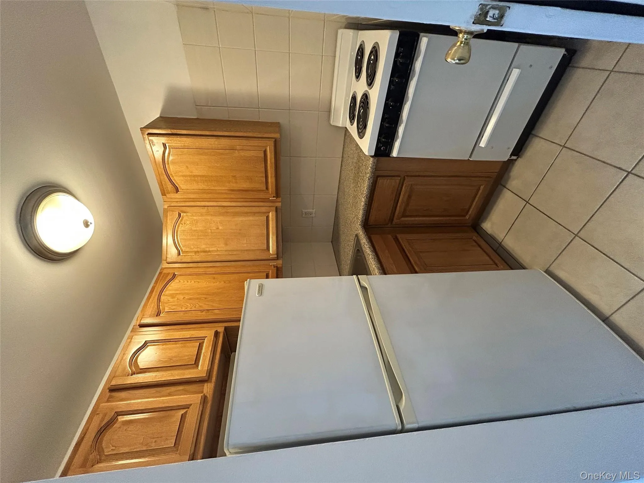 Kitchen with refrigerator, stove, light tile patterned floors, decorative backsplash, and brown cabinets Kitchen with refrigerator, stove, light tile patterned floors, decorative backsplash, and brown cabinets