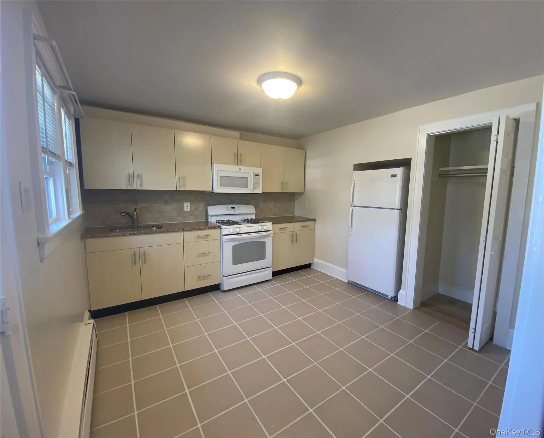 Kitchen featuring backsplash, white appliances, light tile patterned floors, and a baseboard radiator Kitchen featuring backsplash, white appliances, light tile patterned floors, and a baseboard radiator