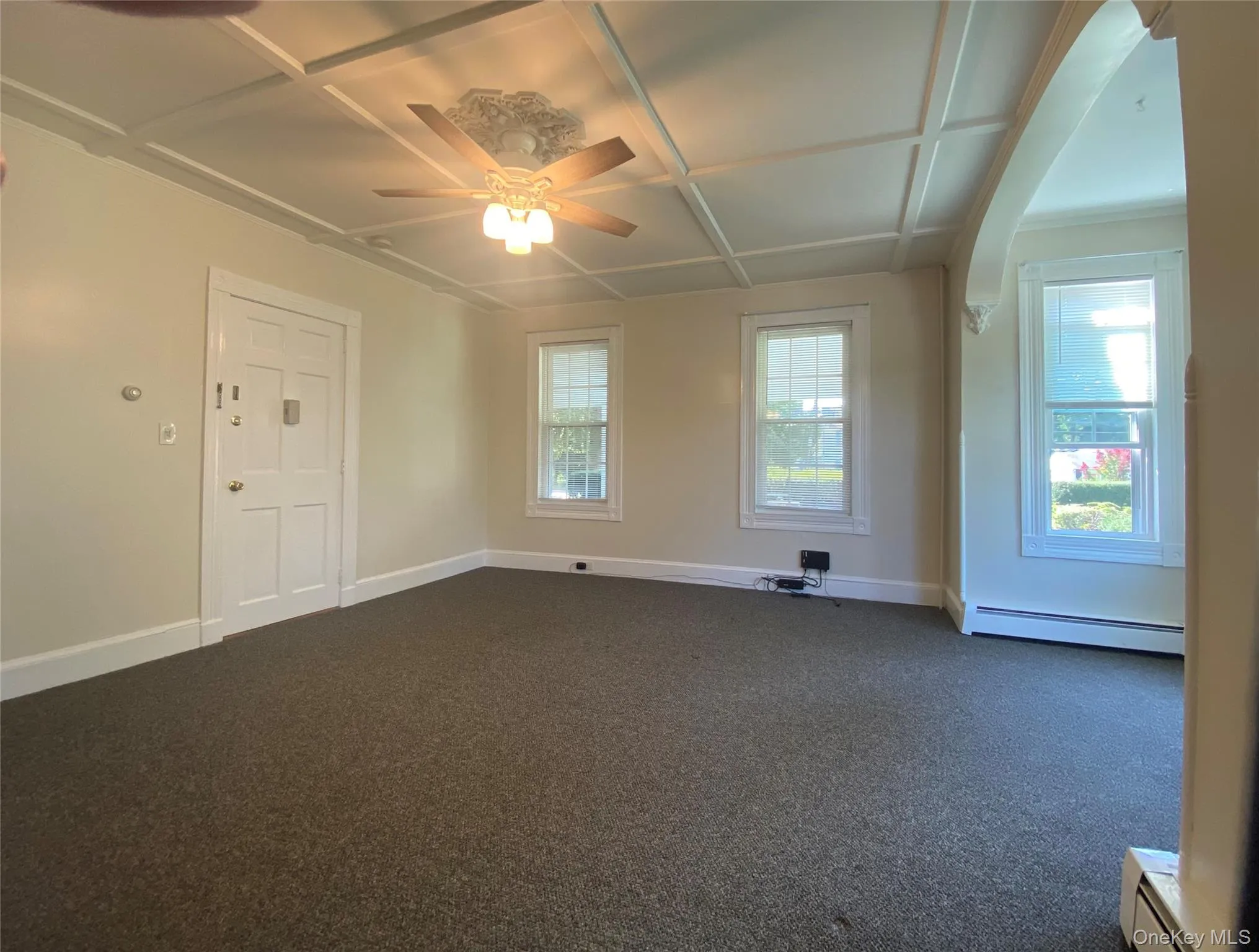 Empty room with dark colored carpet, baseboard heating, and a ceiling fan Empty room with dark colored carpet, baseboard heating, and a ceiling fan