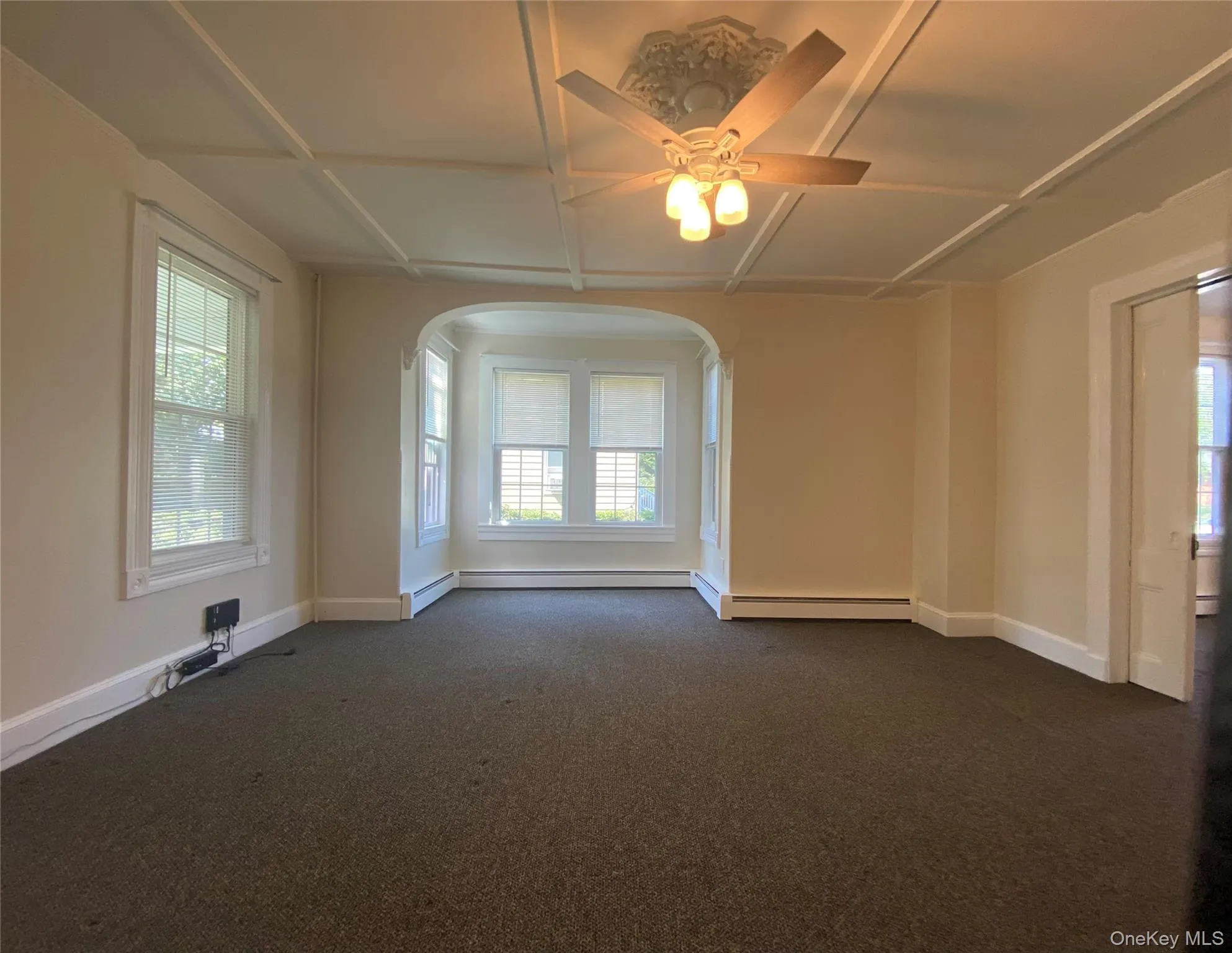 Empty room with plenty of natural light, dark colored carpet, and coffered ceiling Empty room with plenty of natural light, dark colored carpet, and coffered ceiling