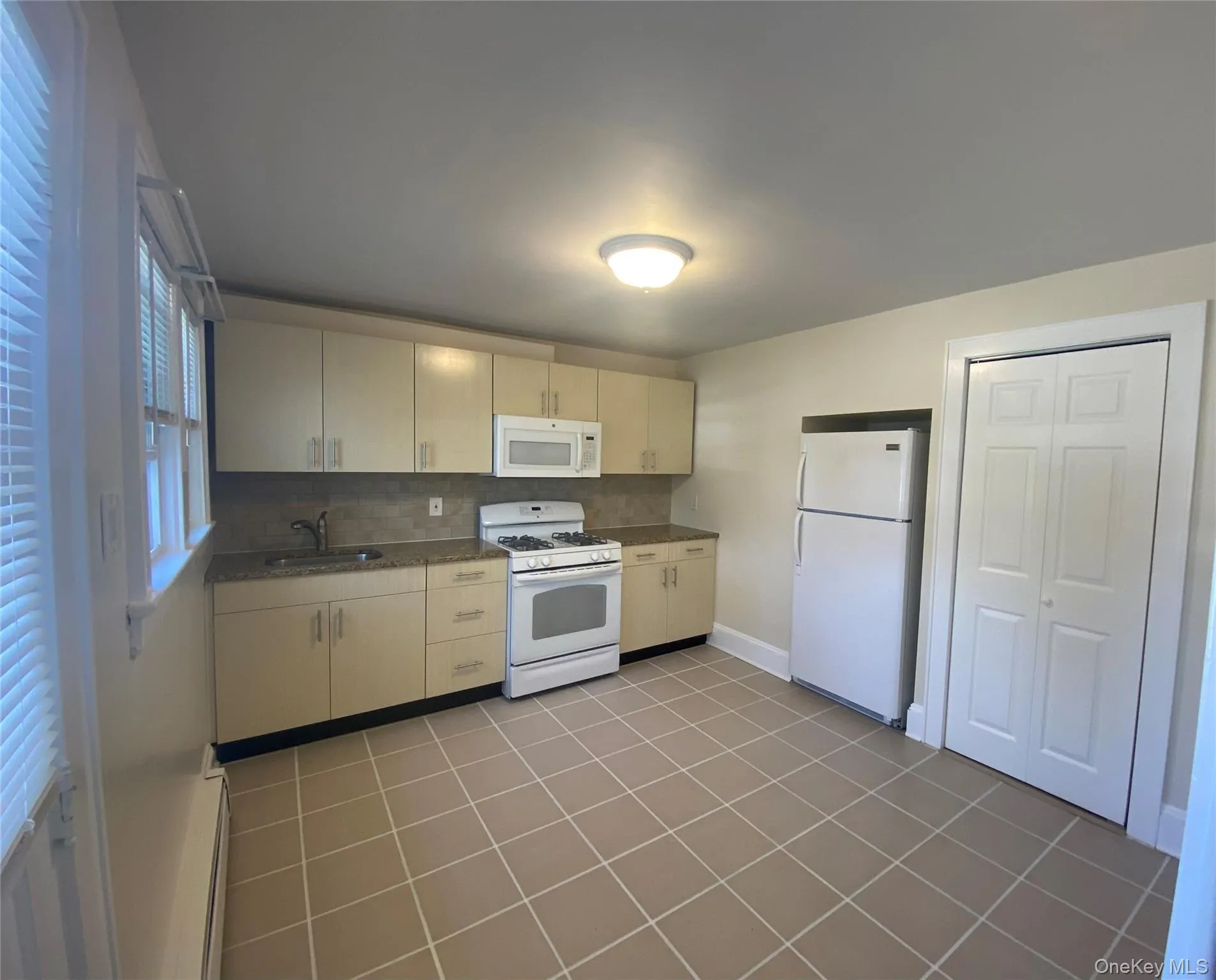 Kitchen with white appliances, decorative backsplash, light tile patterned floors, and a baseboard heating unit Kitchen with white appliances, decorative backsplash, light tile patterned floors, and a baseboard heating unit