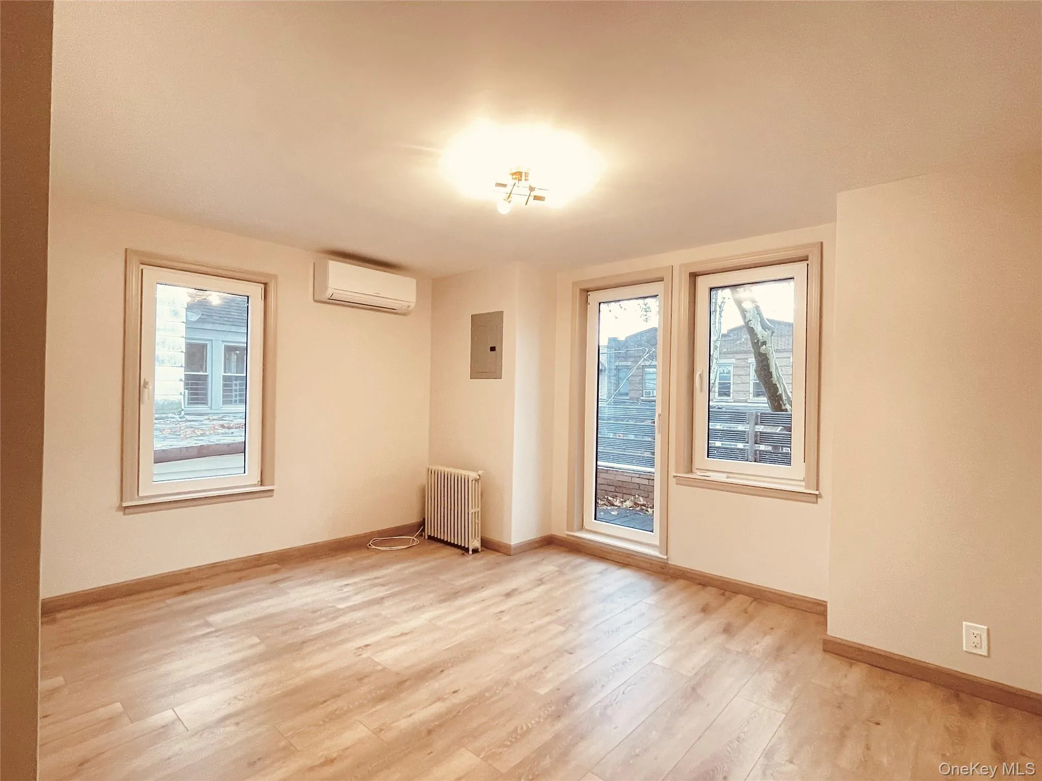 Empty room with light wood finished floors, healthy amount of natural light, radiator, and a wall mounted air conditioner Empty room with light wood finished floors, healthy amount of natural light, radiator, and a wall mounted air conditioner