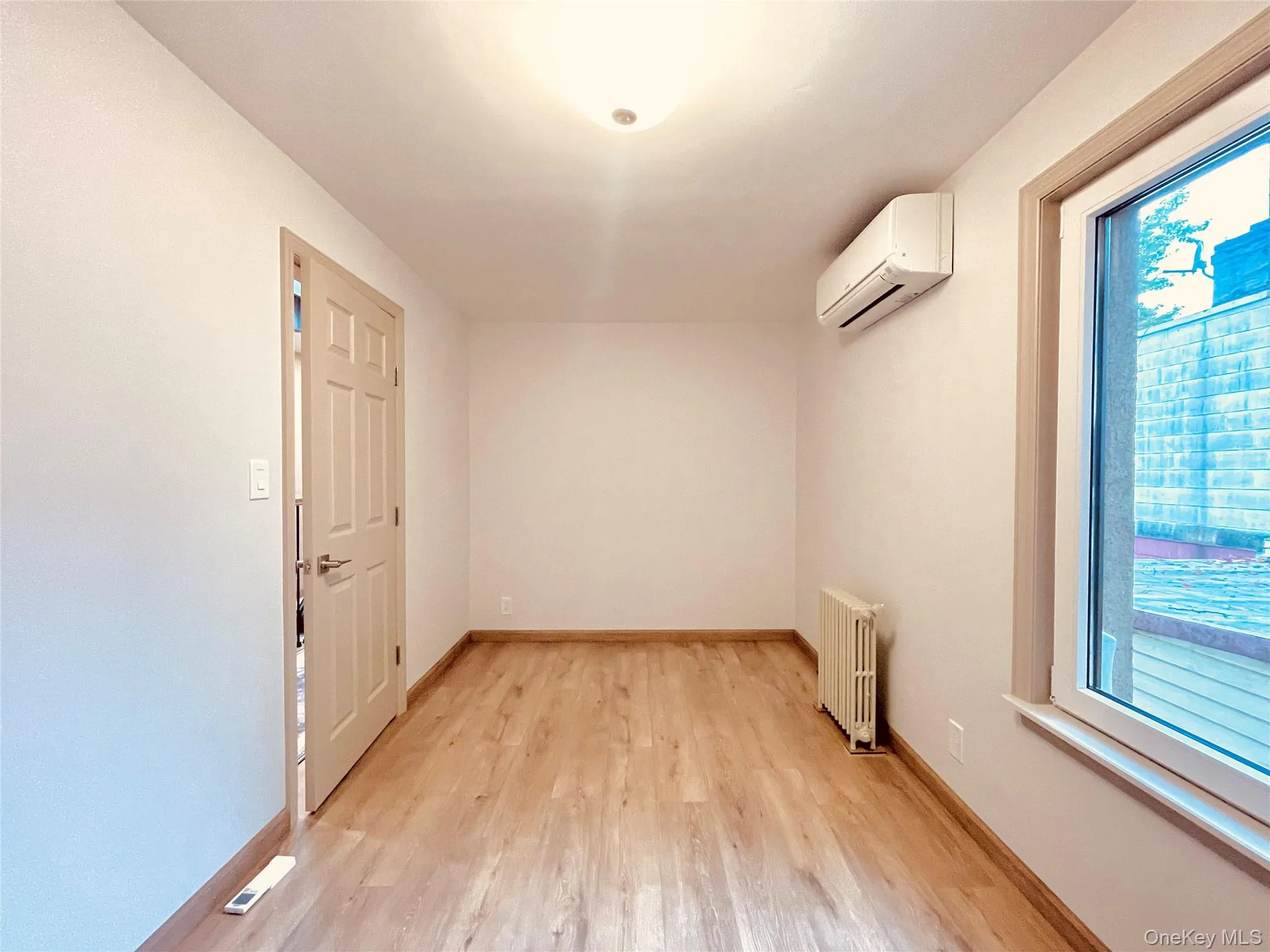 Unfurnished room featuring light wood-style floors, radiator, and a wall mounted air conditioner Unfurnished room featuring light wood-style floors, radiator, and a wall mounted air conditioner