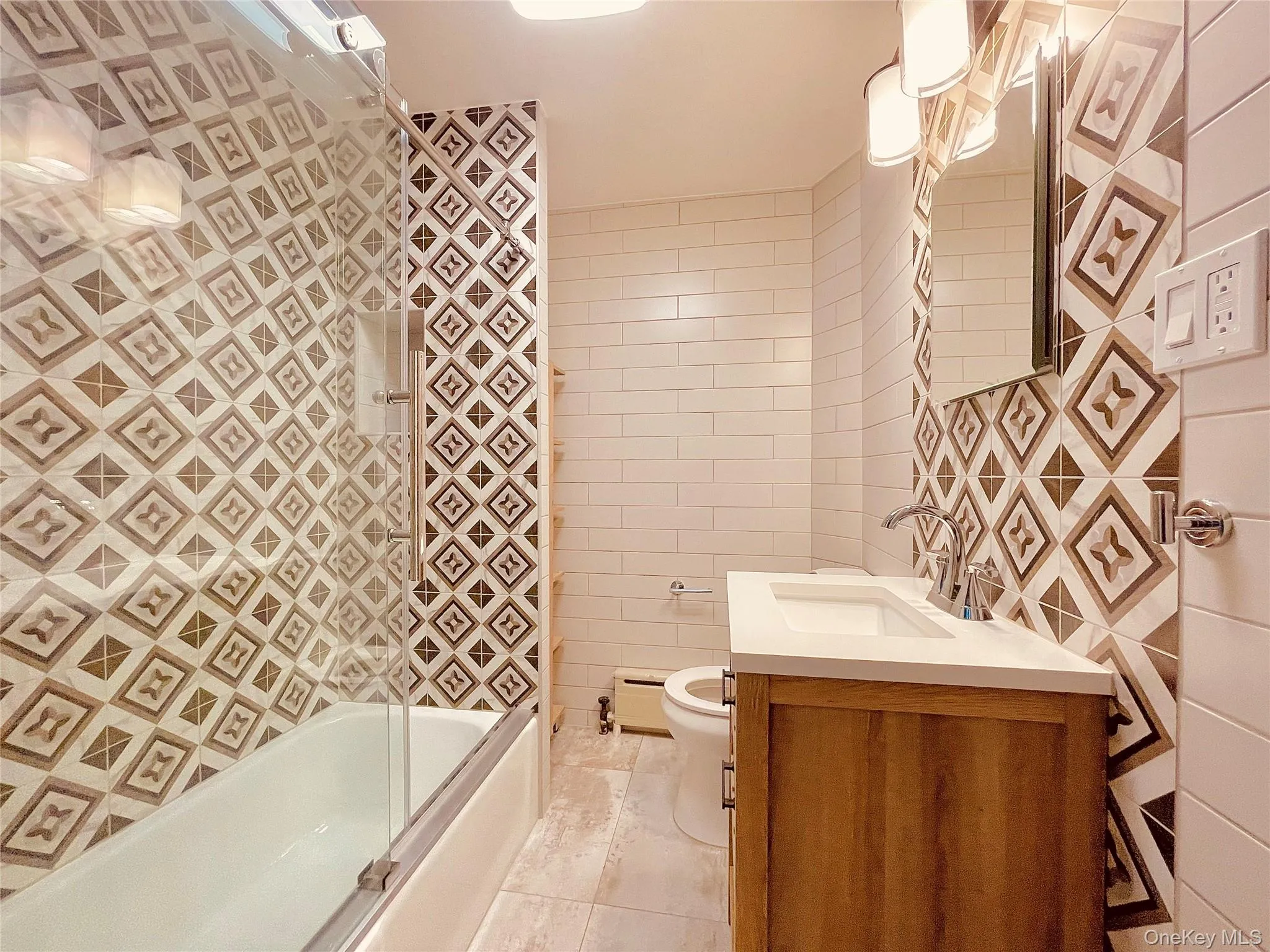Full bathroom featuring tile walls, vanity, bath / shower combo with glass door, baseboard heating, and light tile patterned floors Full bathroom featuring tile walls, vanity, bath / shower combo with glass door, baseboard heating, and light tile patterned floors