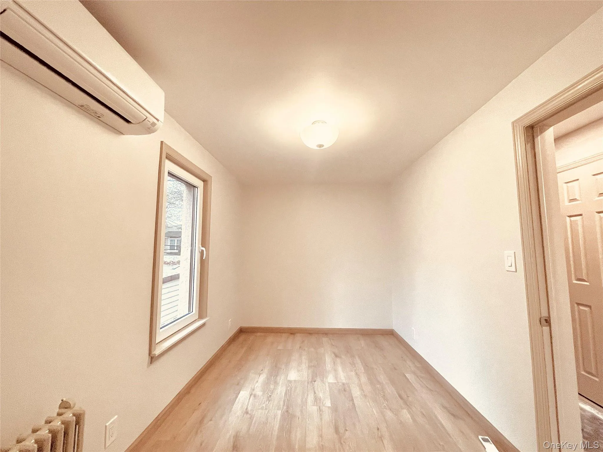 Empty room with a wall unit AC, light wood-style floors, and radiator Empty room with a wall unit AC, light wood-style floors, and radiator