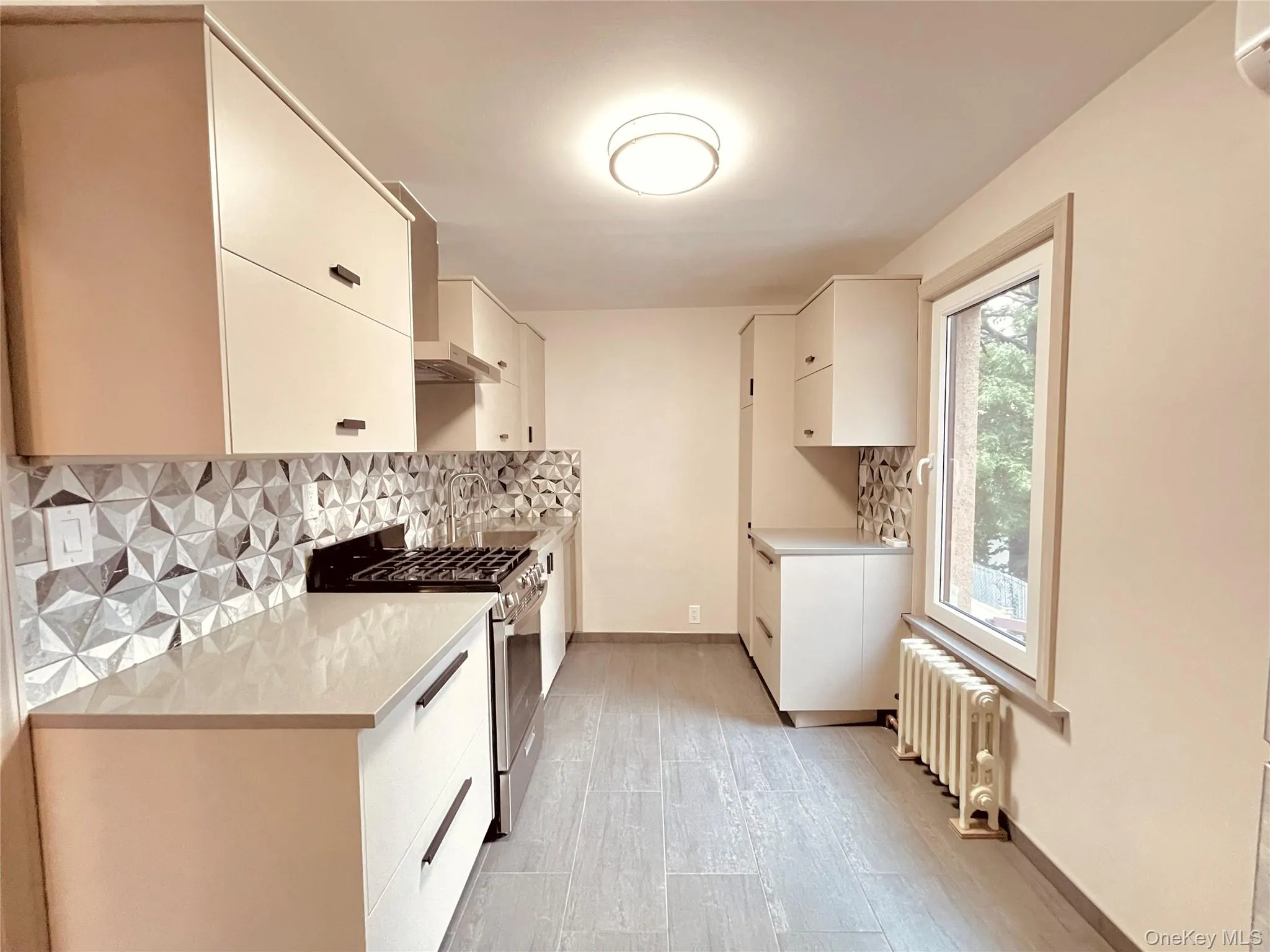 Kitchen featuring decorative backsplash, gas range, radiator heating unit, light wood-style flooring, and wall chimney range hood Kitchen featuring decorative backsplash, gas range, radiator heating unit, light wood-style flooring, and wall chimney range hood