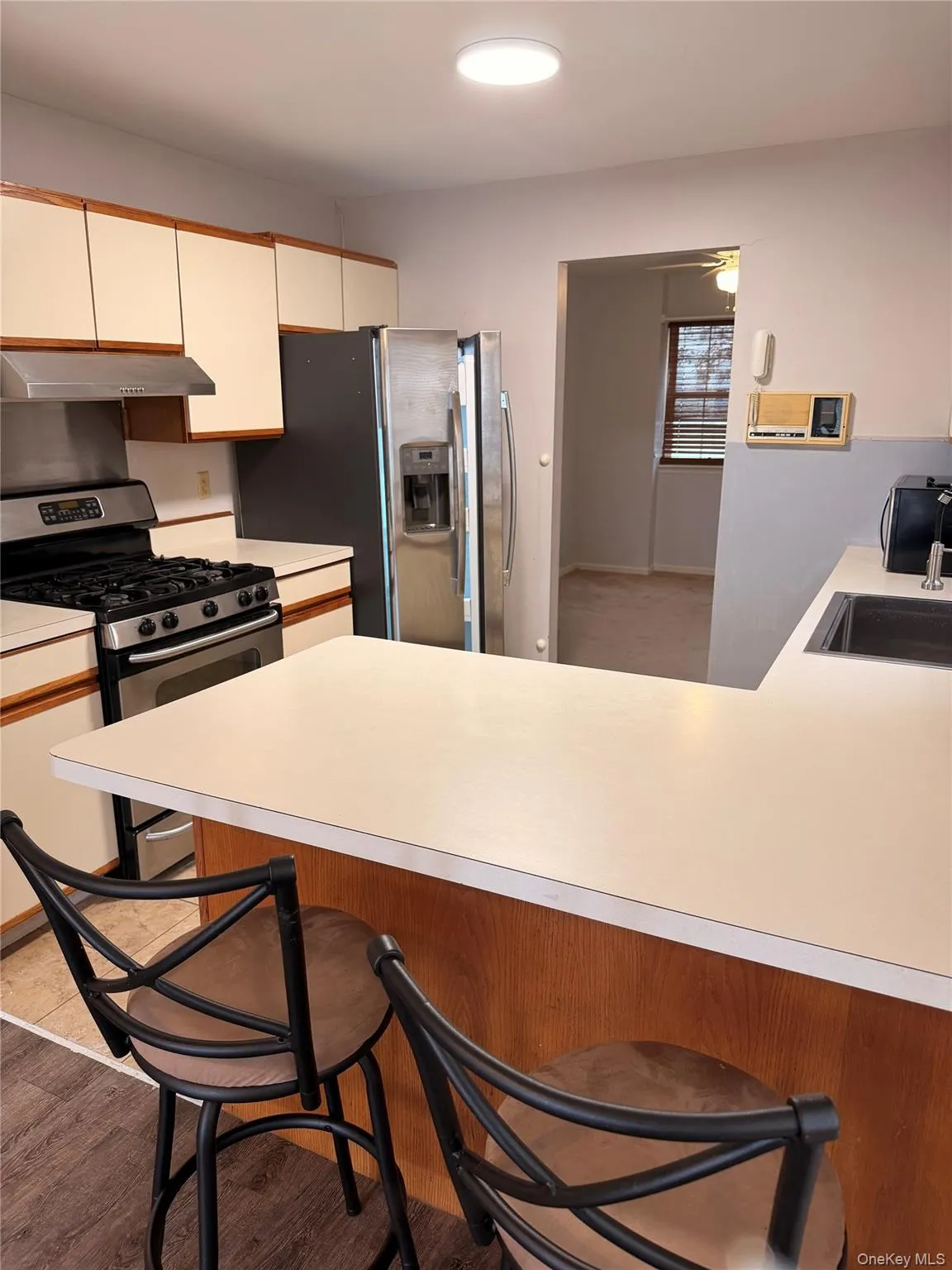 Kitchen with a breakfast bar, stainless steel appliances, light countertops, under cabinet range hood, and light wood finished floors Kitchen with a breakfast bar, stainless steel appliances, light countertops, under cabinet range hood, and light wood finished floors