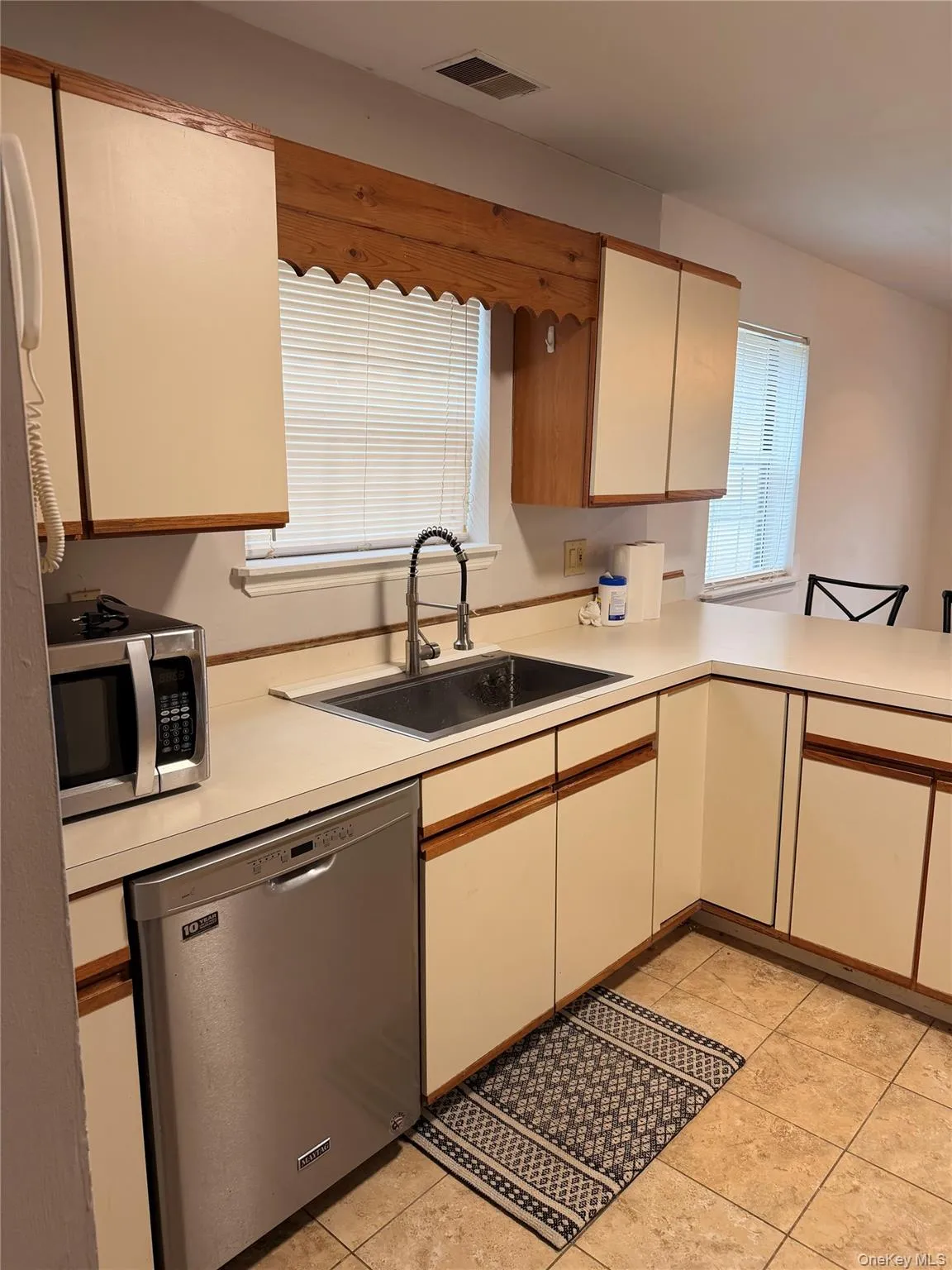 Kitchen with light countertops, appliances with stainless steel finishes, light tile patterned floors, brown cabinetry, and a peninsula Kitchen with light countertops, appliances with stainless steel finishes, light tile patterned floors, brown cabinetry, and a peninsula