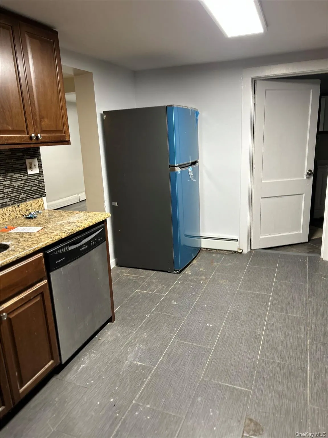 Kitchen featuring freestanding refrigerator, stainless steel dishwasher, light stone countertops, backsplash, and a baseboard heating unit Kitchen featuring freestanding refrigerator, stainless steel dishwasher, light stone countertops, backsplash, and a baseboard heating unit