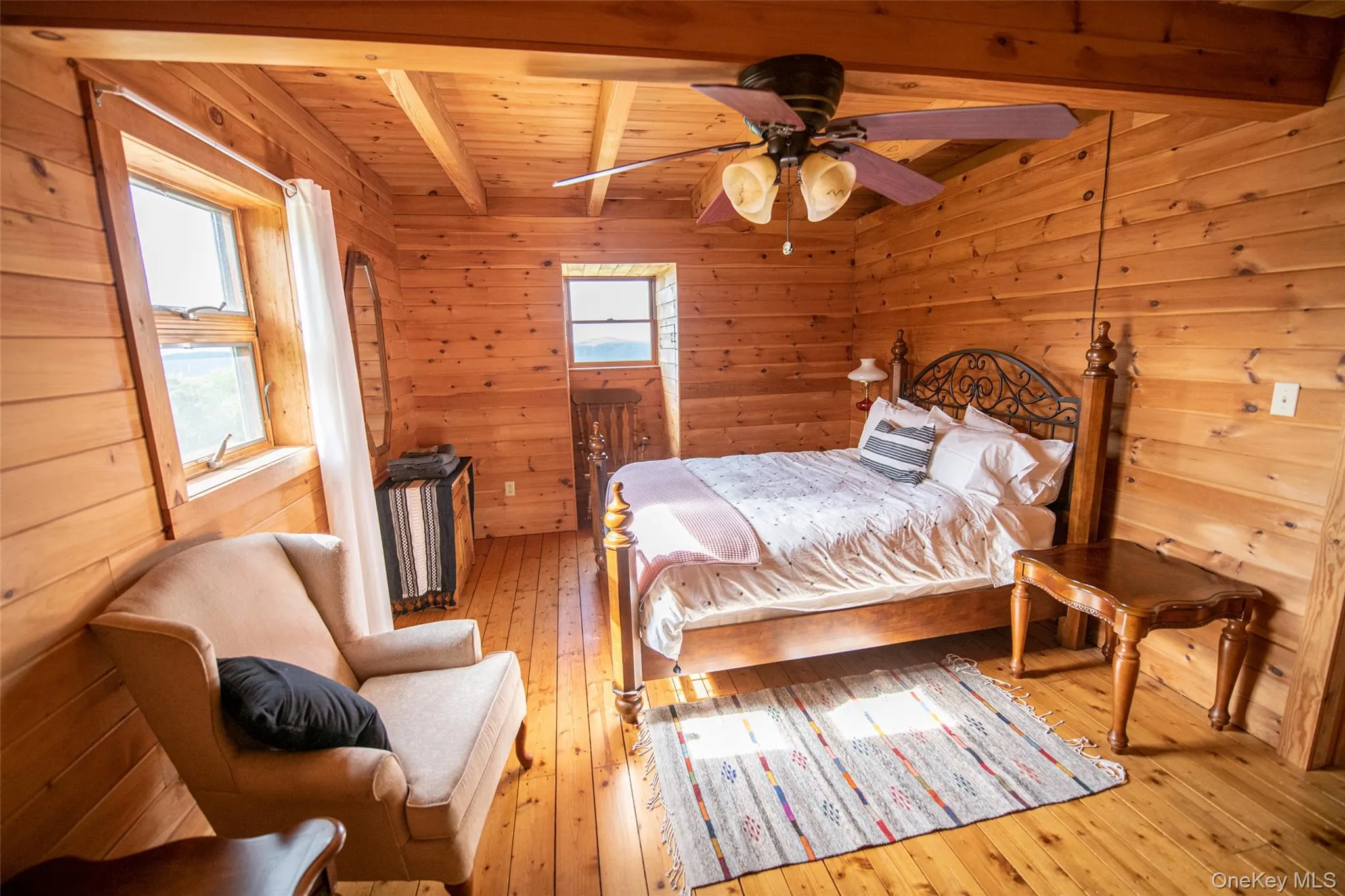 Bedroom featuring light wood-type flooring, wood walls, ceiling fan, and a wood ceiling with exposed beams Bedroom featuring light wood-type flooring, wood walls, ceiling fan, and a wood ceiling with exposed beams