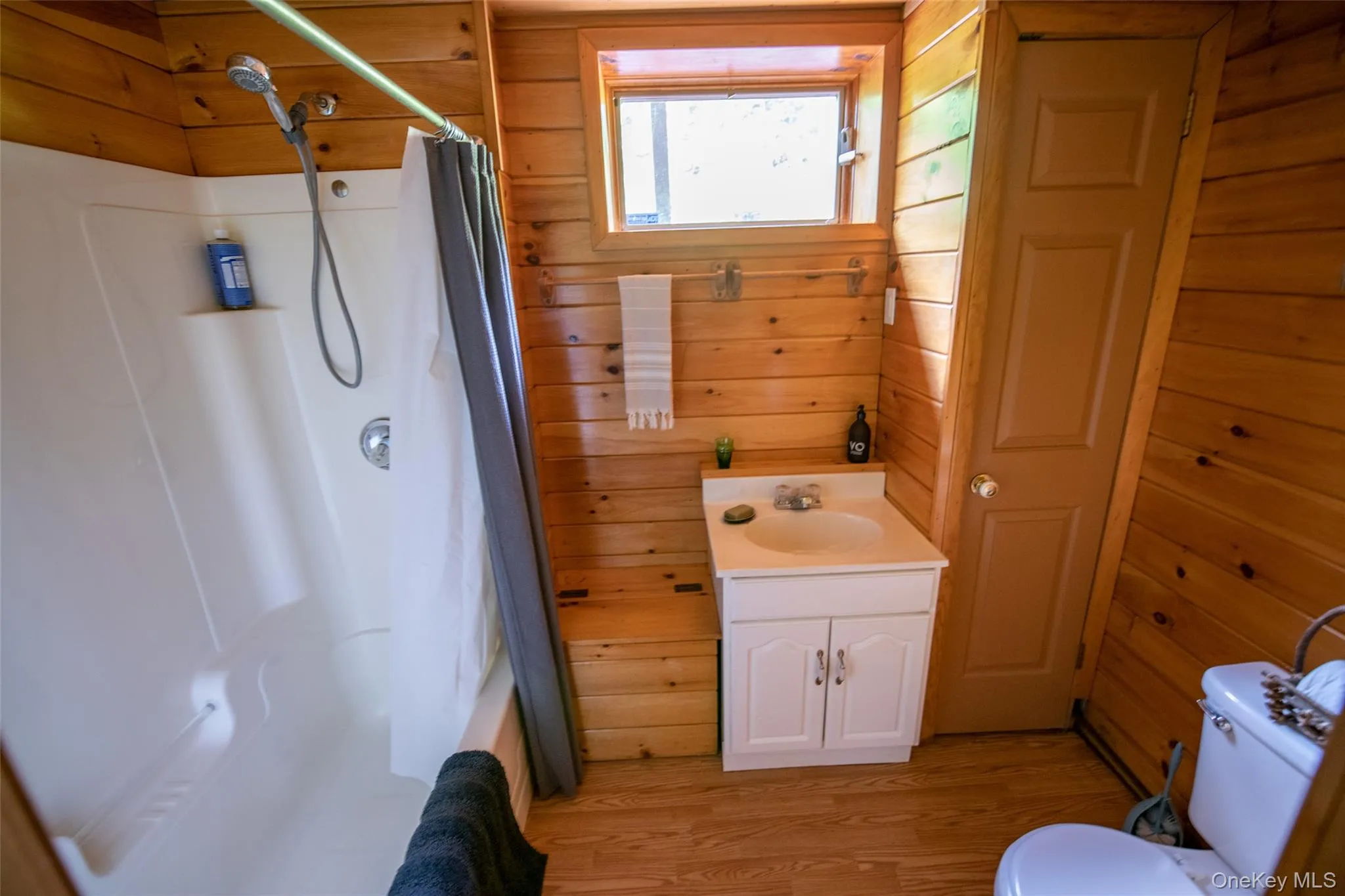 Full bath with wooden walls, vanity, and light wood-type flooring Full bath with wooden walls, vanity, and light wood-type flooring