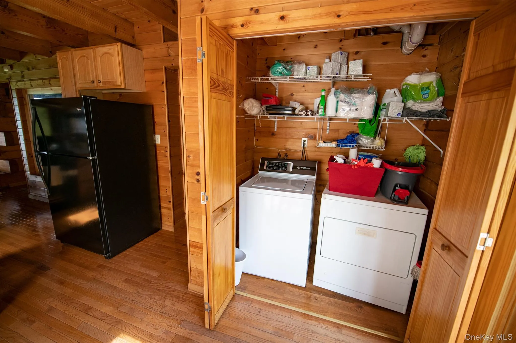 Laundry room with wood walls, light wood-style floors, and washer and clothes dryer Laundry room with wood walls, light wood-style floors, and washer and clothes dryer