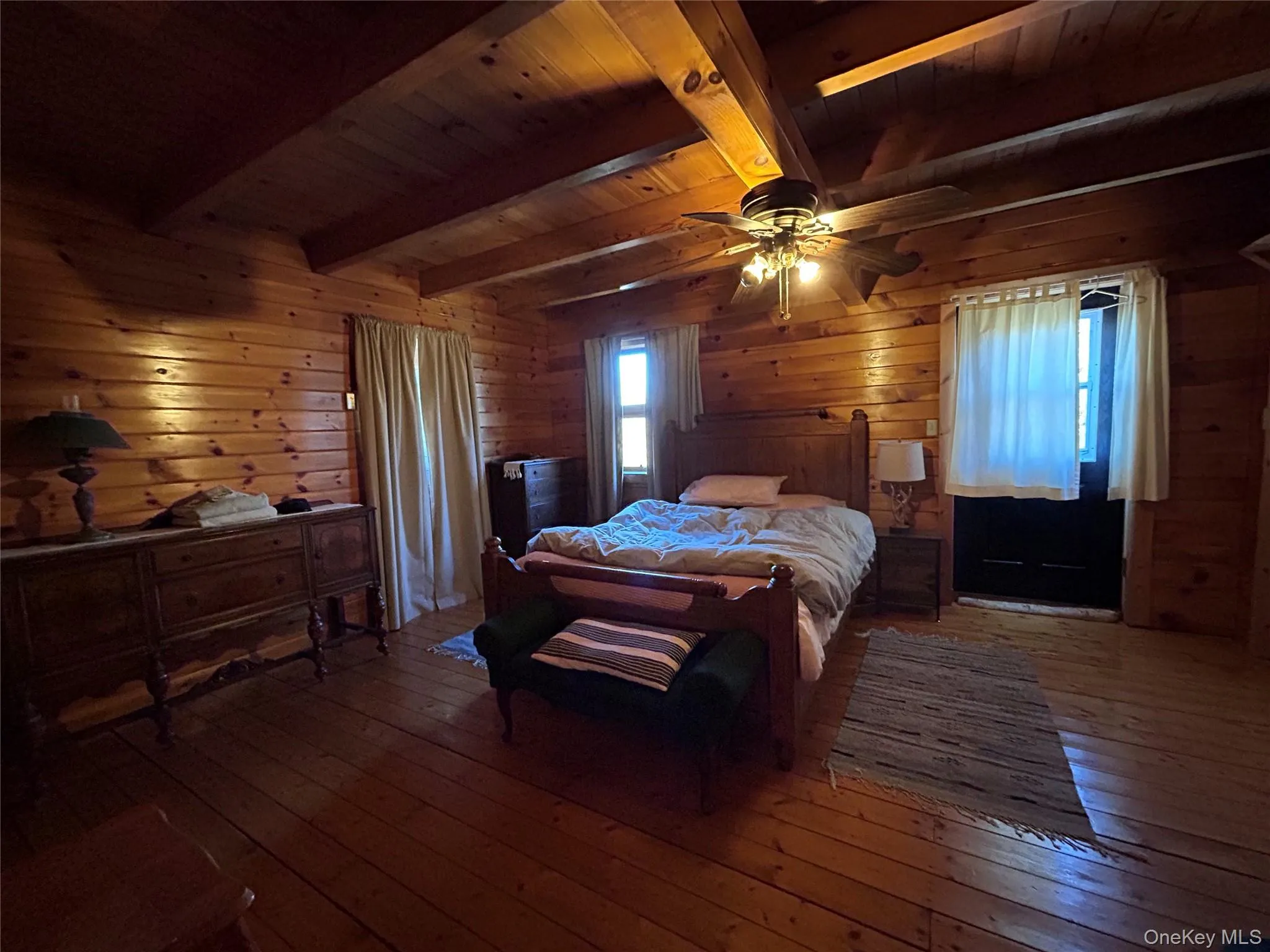 Bedroom featuring hardwood / wood-style floors, wood walls, ceiling fan, and a wooden ceiling with exposed beams Bedroom featuring hardwood / wood-style floors, wood walls, ceiling fan, and a wooden ceiling with exposed beams