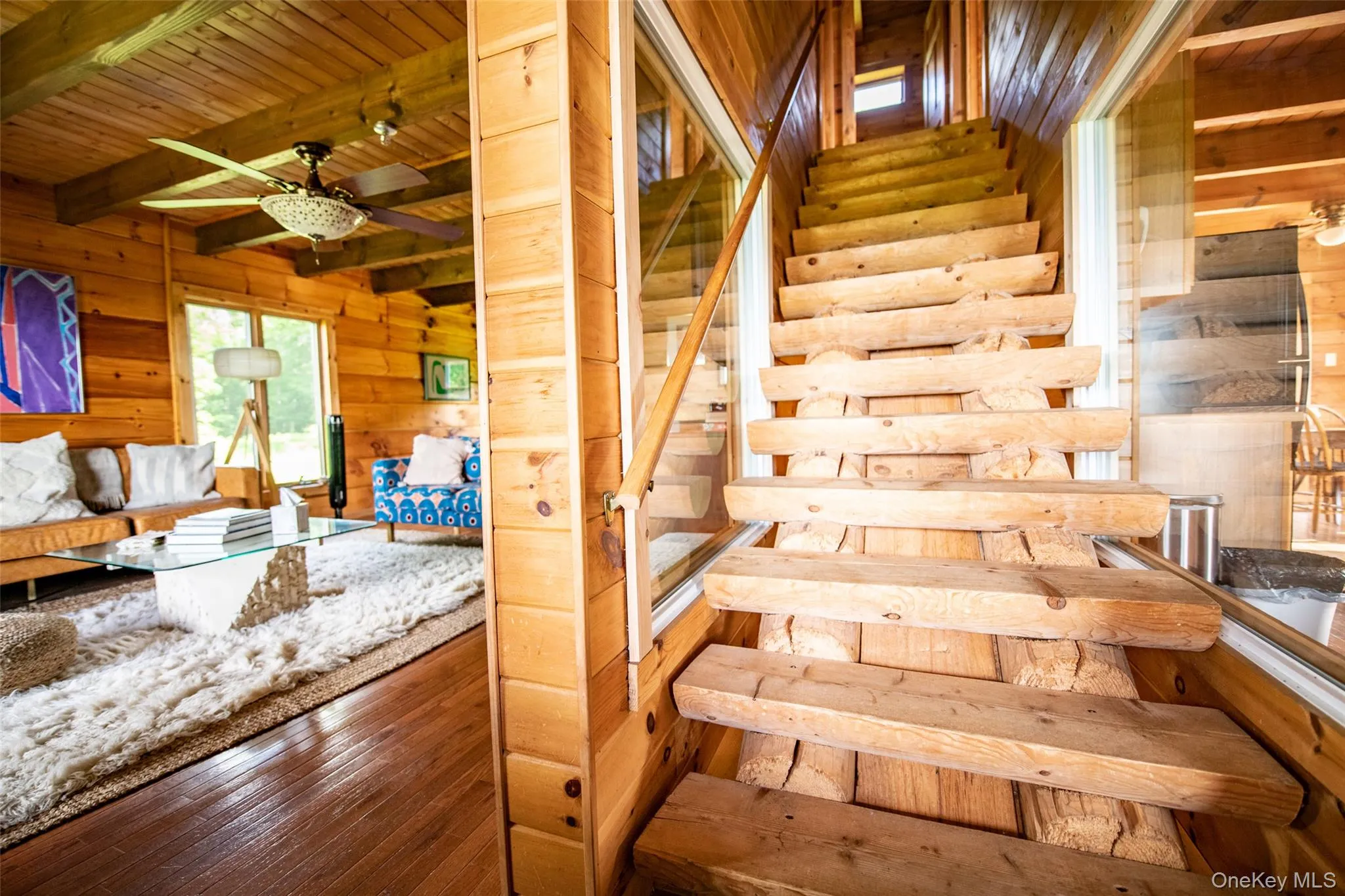 Stairway featuring wood walls, wood-type flooring, a wood ceiling with exposed beams, and a ceiling fan Stairway featuring wood walls, wood-type flooring, a wood ceiling with exposed beams, and a ceiling fan