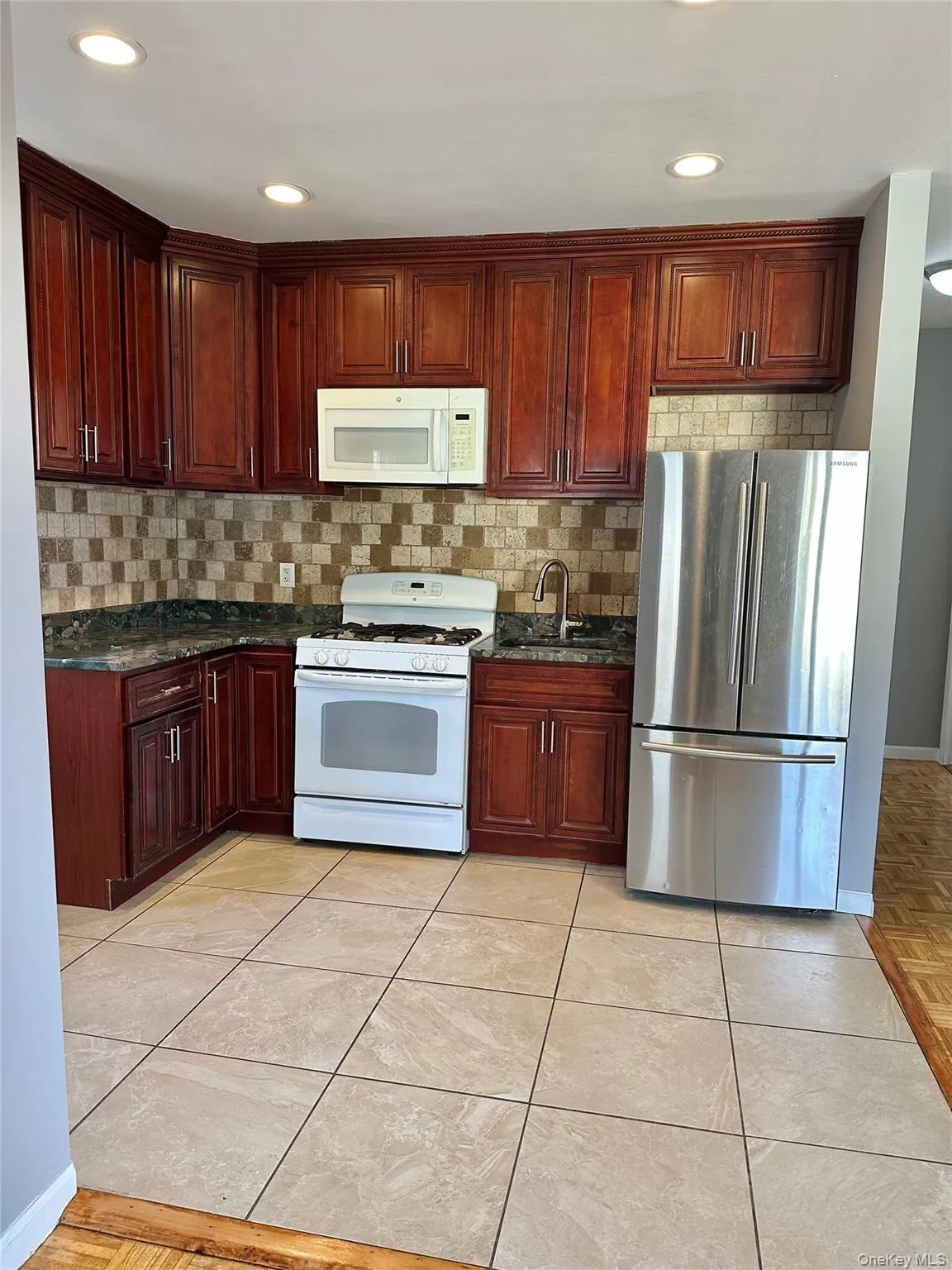 Kitchen featuring white appliances, dark stone countertops, reddish brown cabinets, tasteful backsplash, and recessed lighting Kitchen featuring white appliances, dark stone countertops, reddish brown cabinets, tasteful backsplash, and recessed lighting