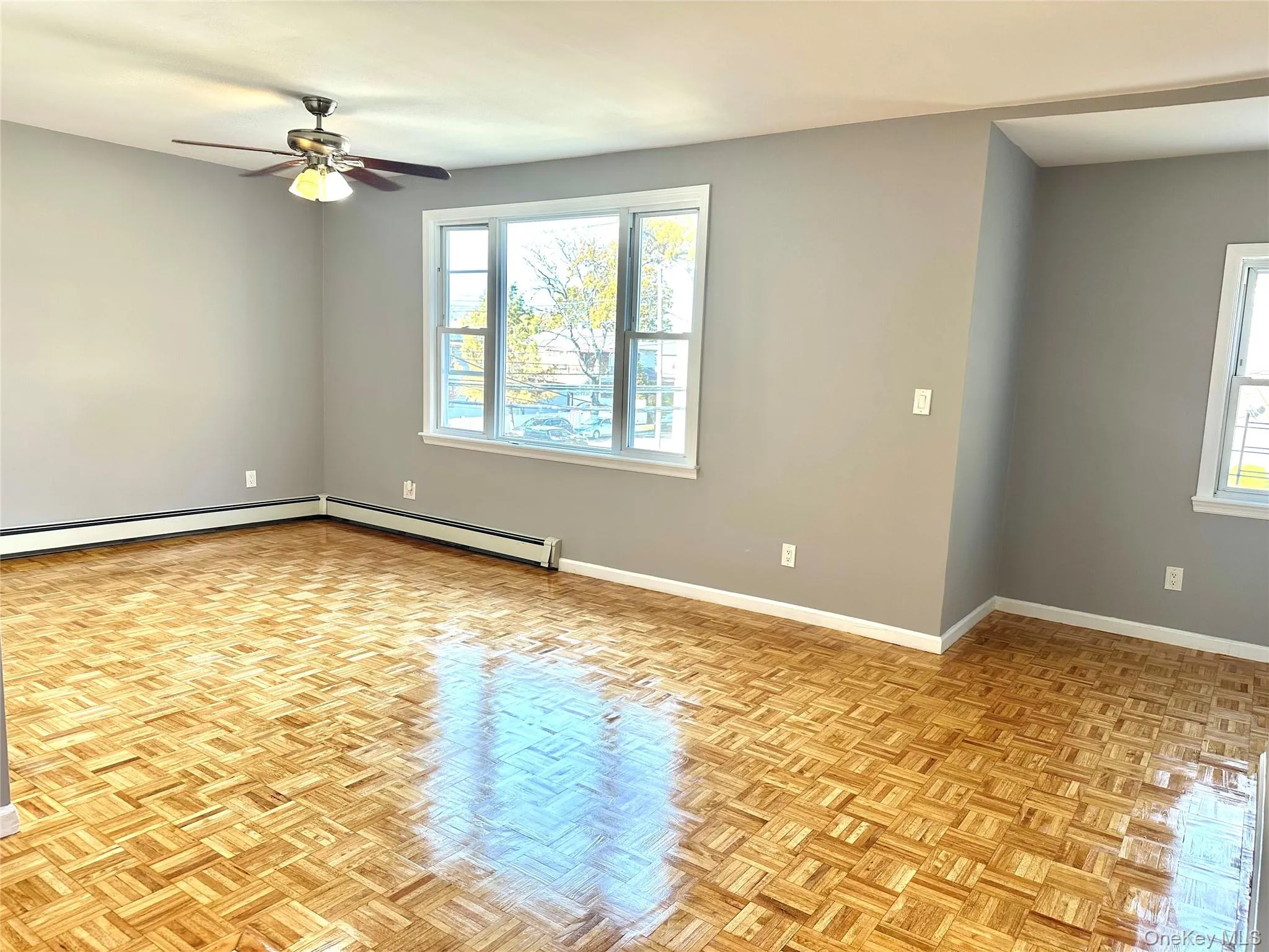 Empty room featuring plenty of natural light, a baseboard radiator, and a ceiling fan Empty room featuring plenty of natural light, a baseboard radiator, and a ceiling fan
