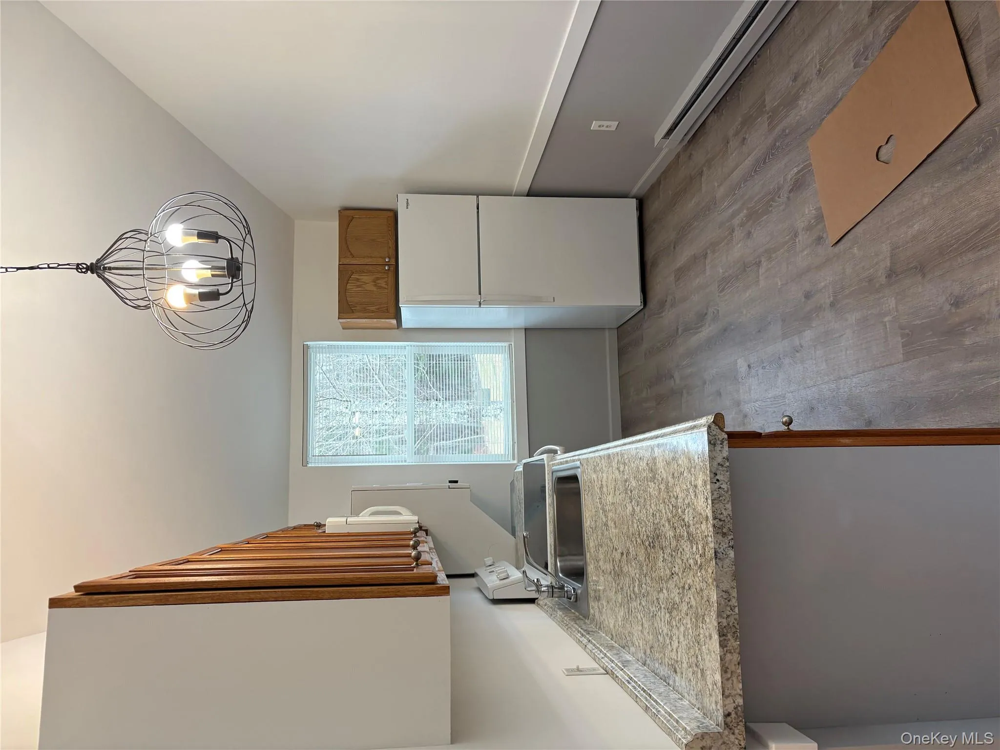 Kitchen featuring brown cabinetry, a baseboard radiator, refrigerator, light wood finished floors, and light countertops Kitchen featuring brown cabinetry, a baseboard radiator, refrigerator, light wood finished floors, and light countertops