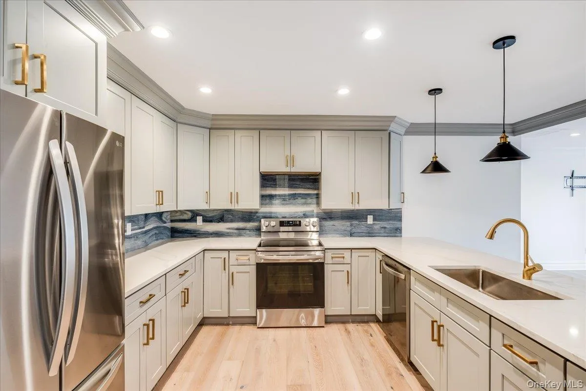 Kitchen with stainless steel appliances, light wood-style floors, backsplash, decorative light fixtures, and light stone countertops Kitchen with stainless steel appliances, light wood-style floors, backsplash, decorative light fixtures, and light stone countertops