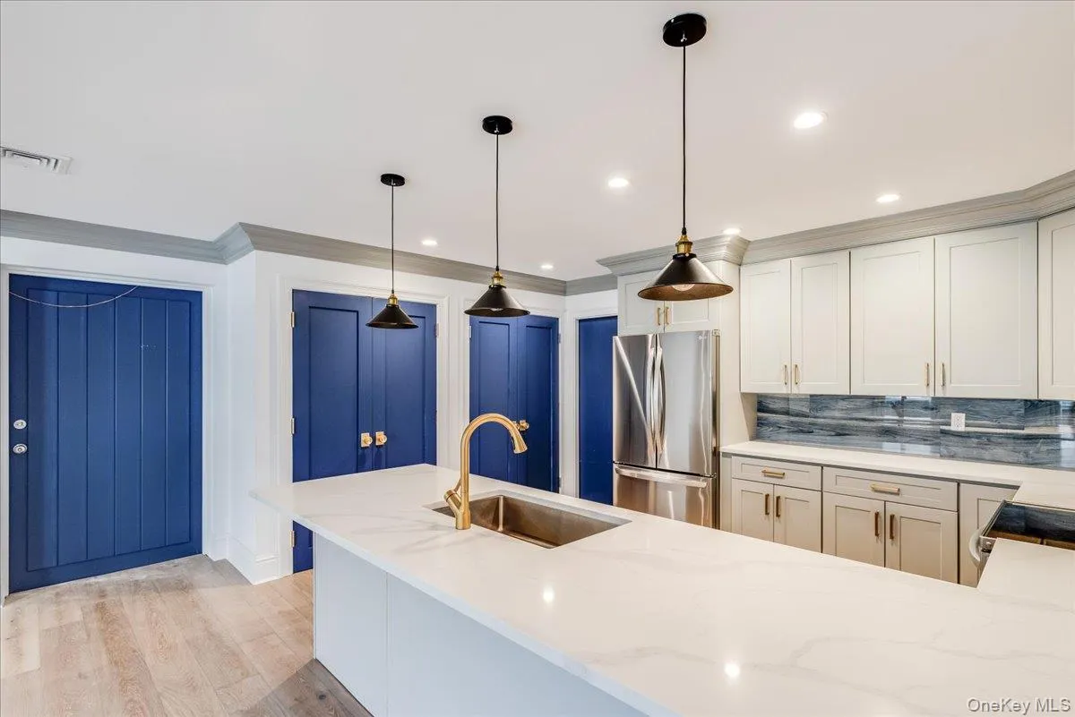 Kitchen featuring stainless steel appliances, ornamental molding, light stone countertops, light wood-type flooring, and backsplash Kitchen featuring stainless steel appliances, ornamental molding, light stone countertops, light wood-type flooring, and backsplash