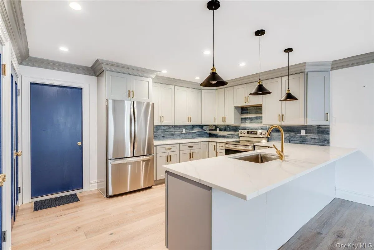 Kitchen featuring stainless steel appliances, decorative backsplash, a peninsula, crown molding, and light stone counters Kitchen featuring stainless steel appliances, decorative backsplash, a peninsula, crown molding, and light stone counters
