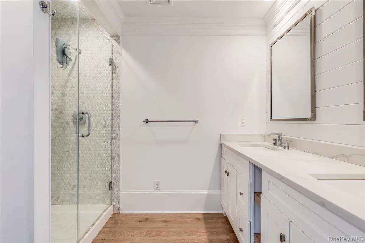 Bathroom with light wood-style flooring, a shower stall, crown molding, and double vanity Bathroom with light wood-style flooring, a shower stall, crown molding, and double vanity