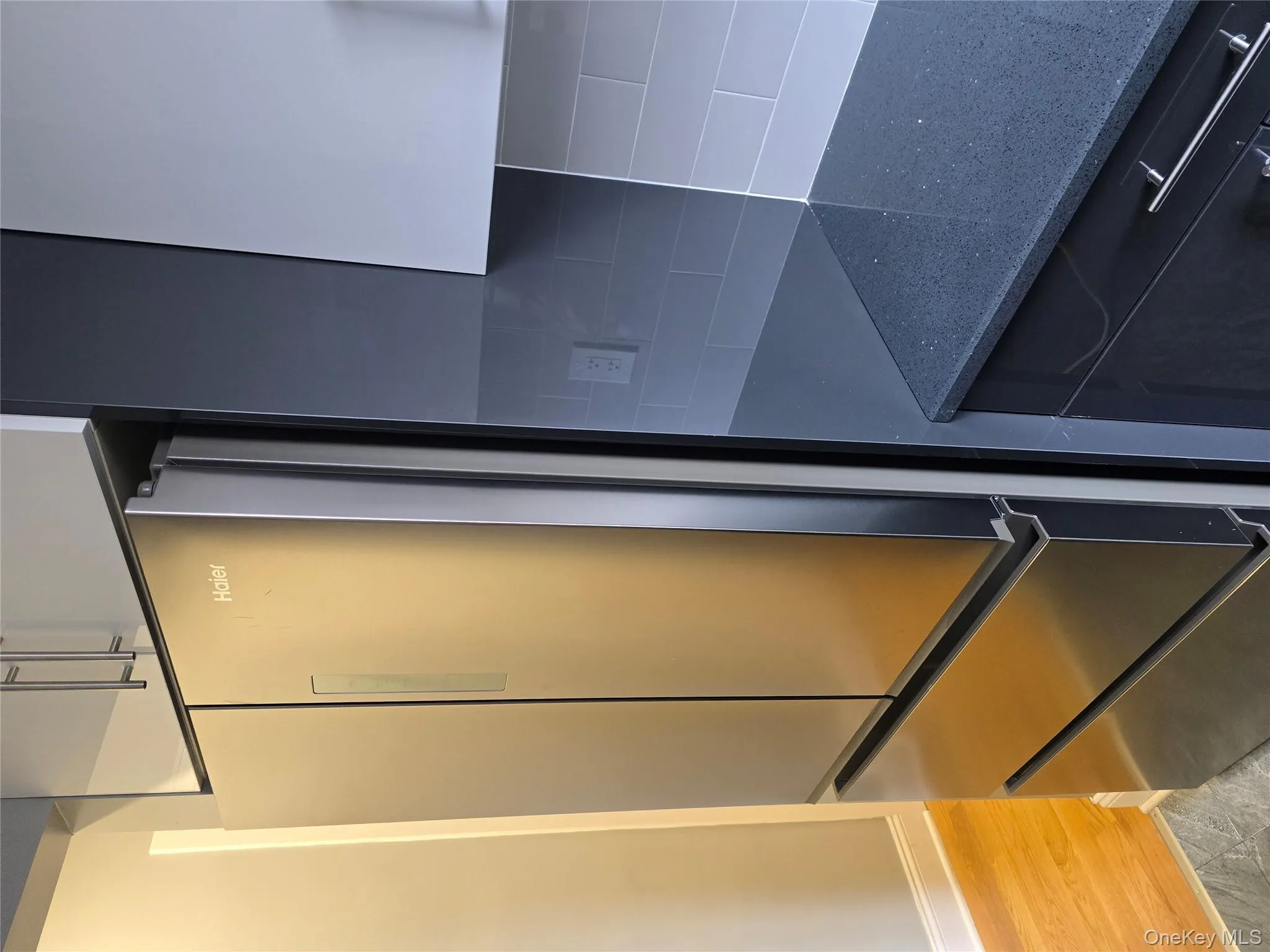 Kitchen view of dark stone countertops, refrigerator, light wood-style flooring, and white cabinets Kitchen view of dark stone countertops, refrigerator, light wood-style flooring, and white cabinets