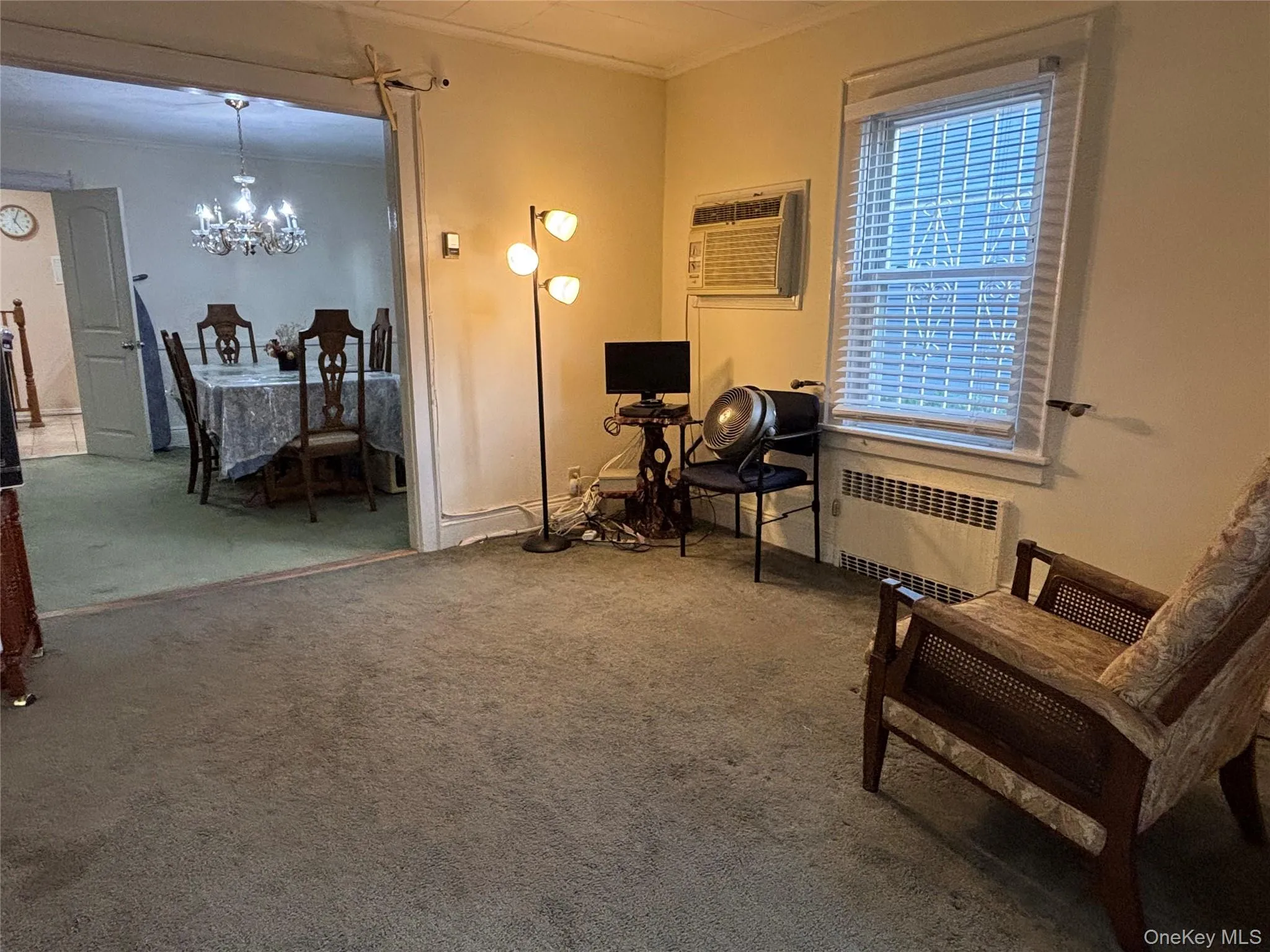 Living area featuring carpet, radiator, a chandelier, a wall unit AC, and ornamental molding Living area featuring carpet, radiator, a chandelier, a wall unit AC, and ornamental molding