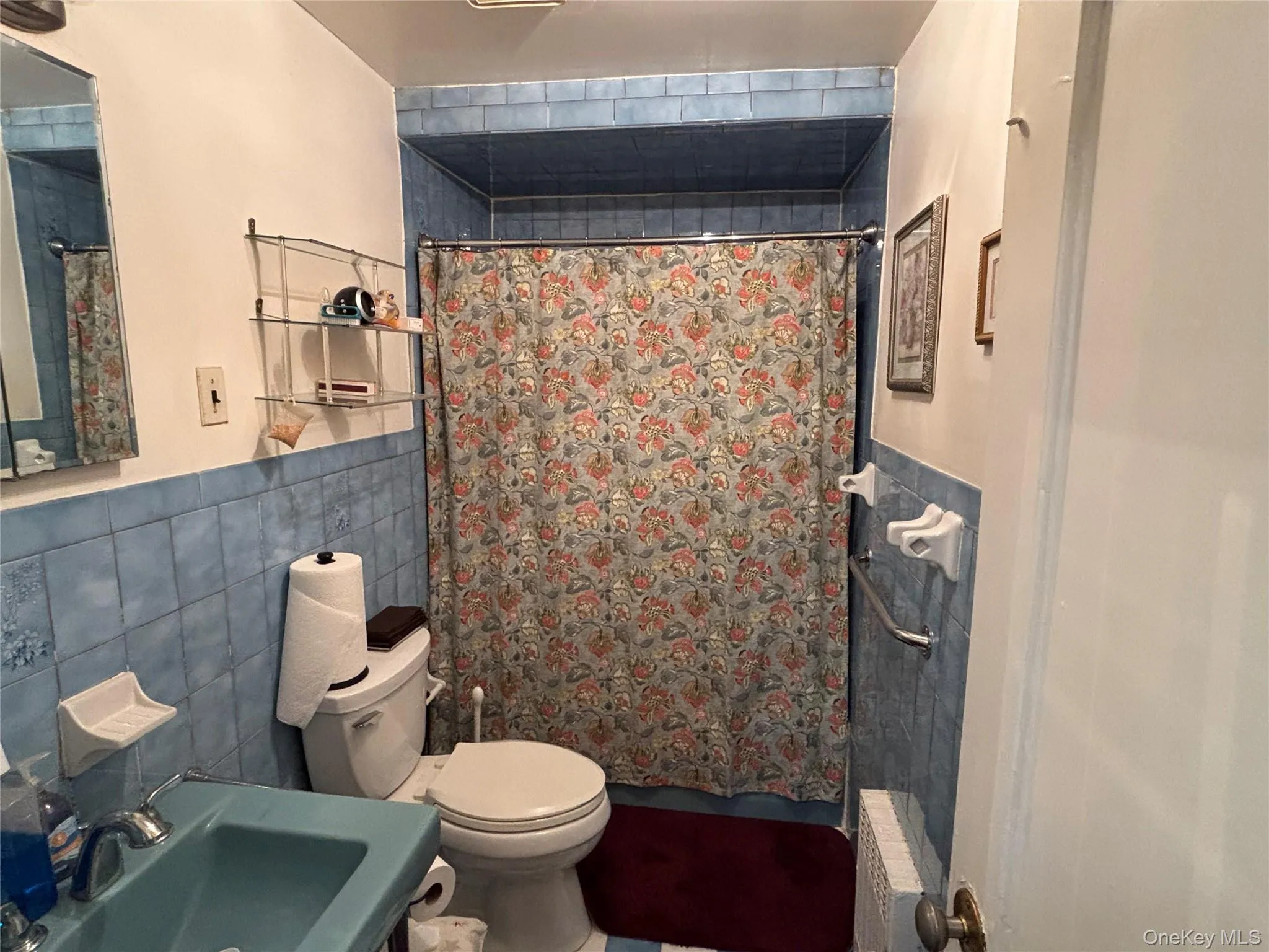 Bathroom featuring tile walls, curtained shower, radiator, a wainscoted wall, and vanity Bathroom featuring tile walls, curtained shower, radiator, a wainscoted wall, and vanity