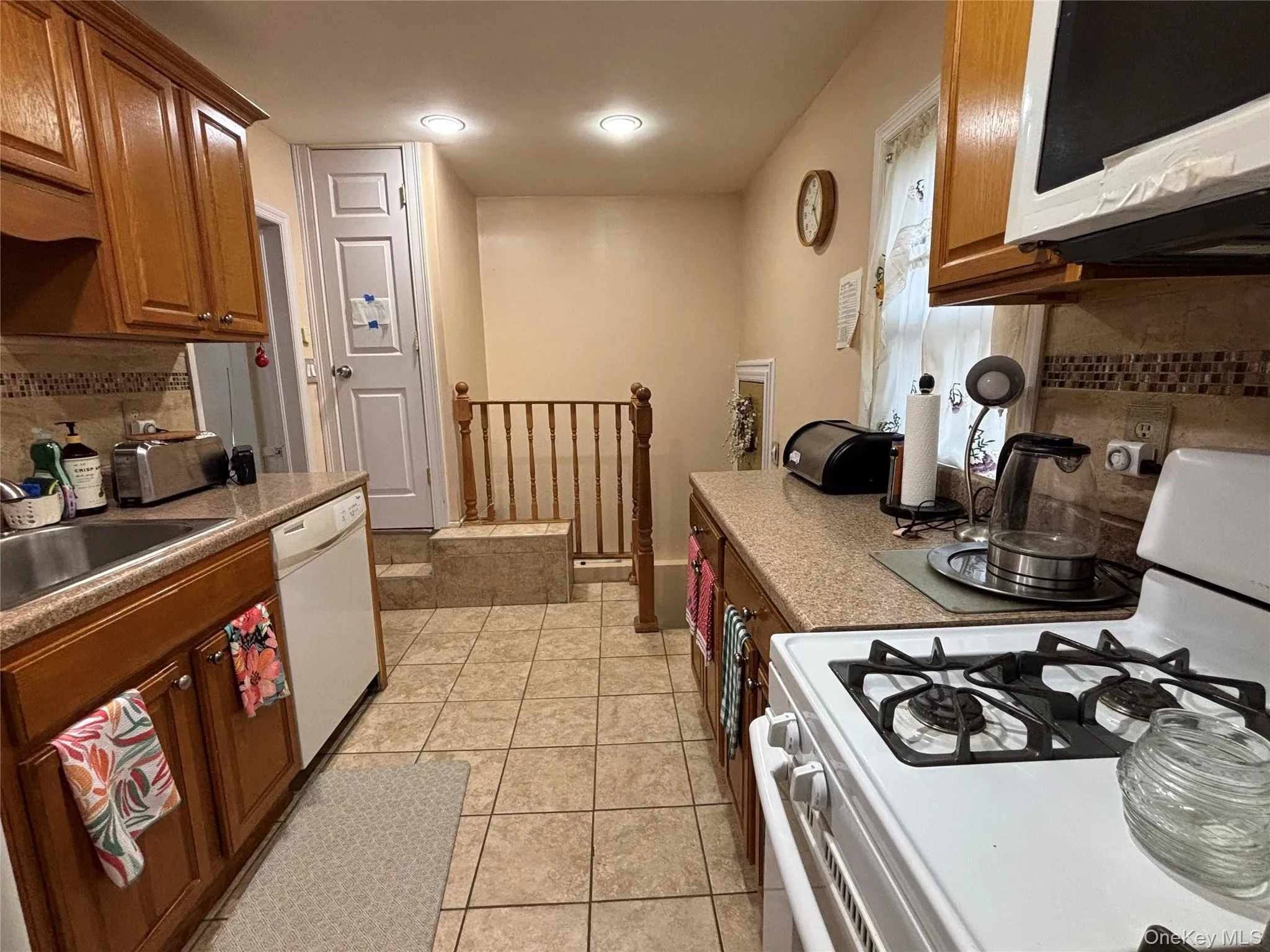 Kitchen featuring tasteful backsplash, white appliances, light tile patterned floors, and brown cabinets Kitchen featuring tasteful backsplash, white appliances, light tile patterned floors, and brown cabinets