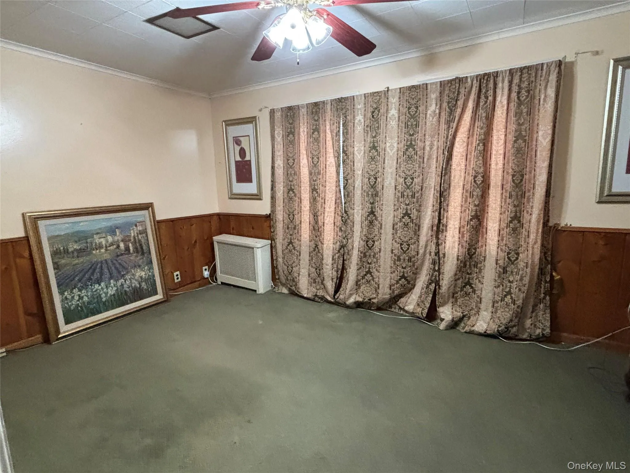 Empty room featuring wooden walls, a wainscoted wall, ornamental molding, carpet, and ceiling fan Empty room featuring wooden walls, a wainscoted wall, ornamental molding, carpet, and ceiling fan