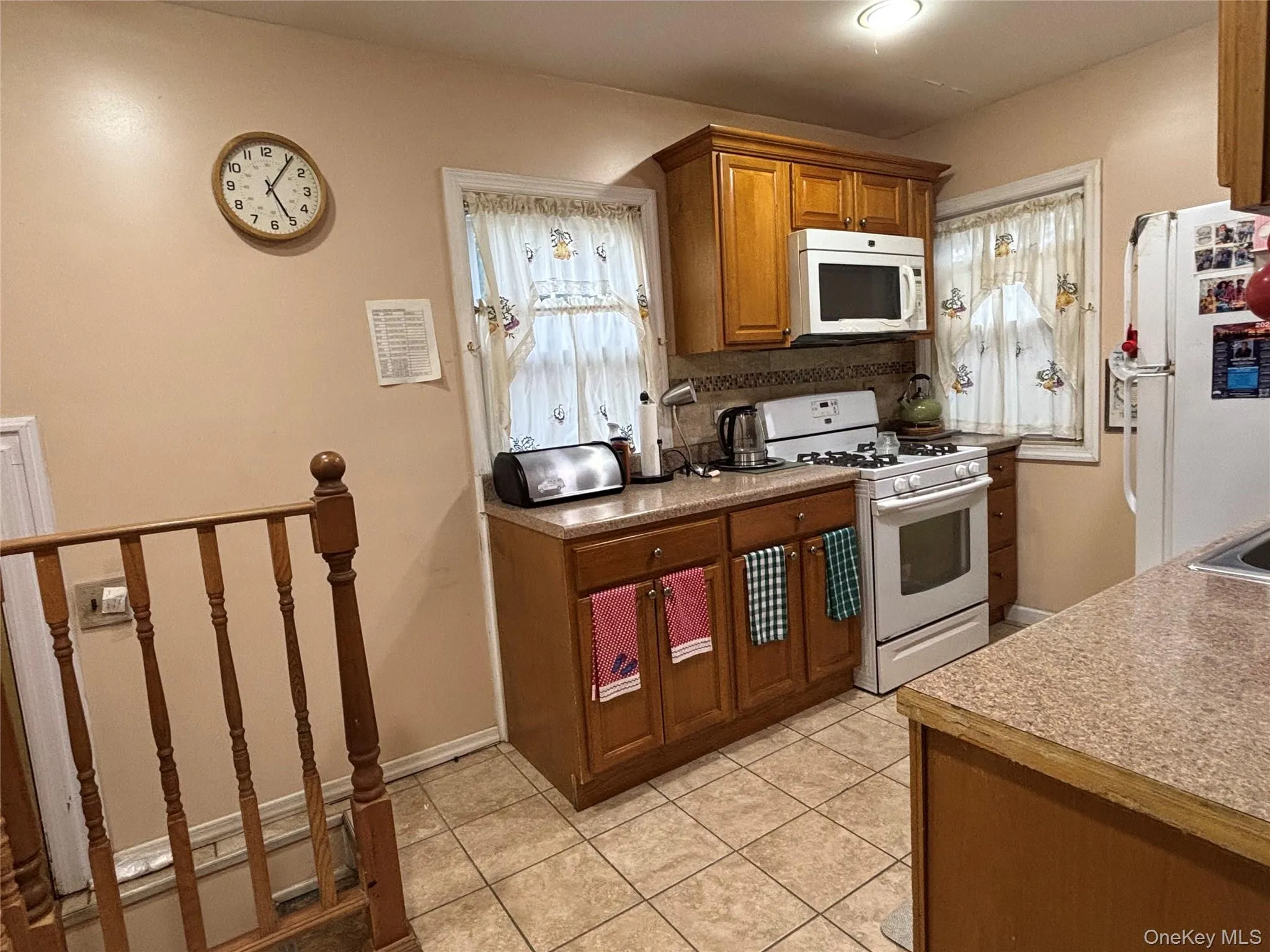 Kitchen with white appliances, light tile patterned floors, brown cabinets, light countertops, and backsplash Kitchen with white appliances, light tile patterned floors, brown cabinets, light countertops, and backsplash