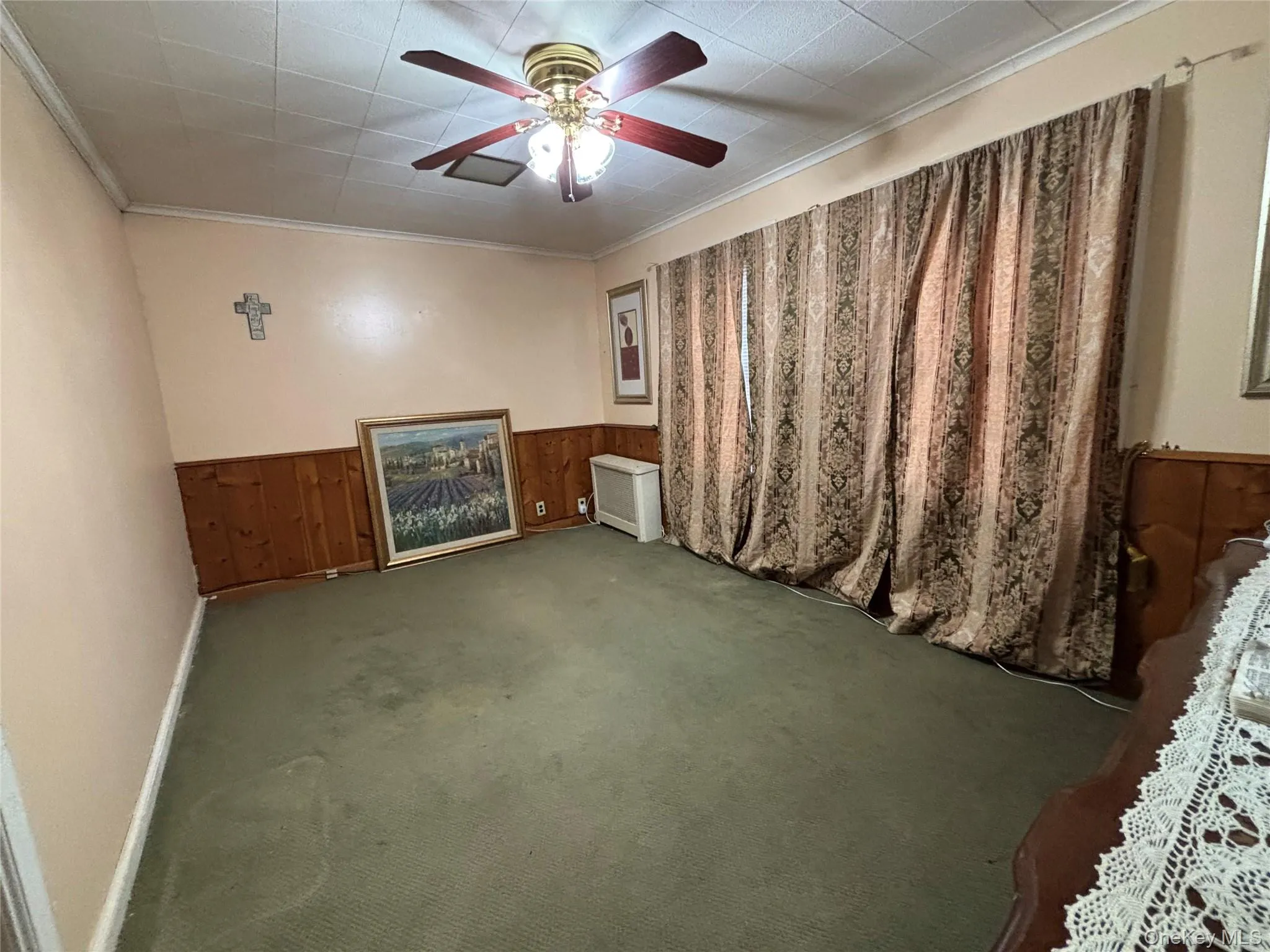 Carpeted empty room featuring wooden walls, ornamental molding, wainscoting, and a ceiling fan Carpeted empty room featuring wooden walls, ornamental molding, wainscoting, and a ceiling fan