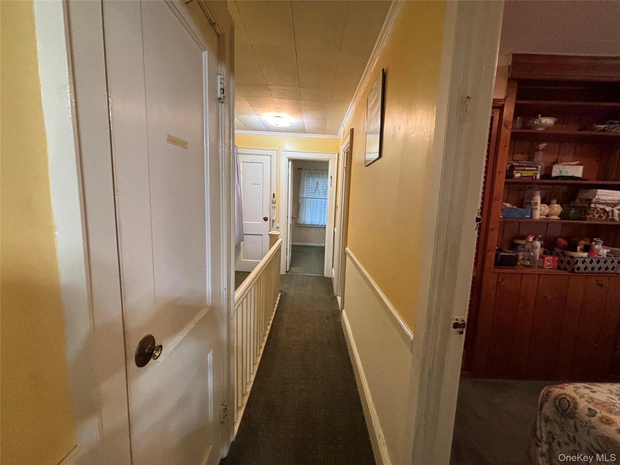 Hallway featuring ornamental molding, dark colored carpet, an upstairs landing, and a wainscoted wall Hallway featuring ornamental molding, dark colored carpet, an upstairs landing, and a wainscoted wall