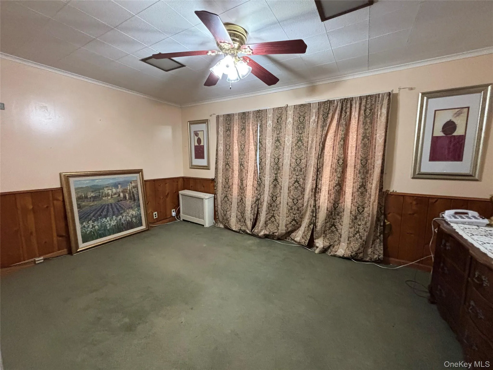 Unfurnished bedroom with wood walls, ornamental molding, a wainscoted wall, a ceiling fan, and carpet Unfurnished bedroom with wood walls, ornamental molding, a wainscoted wall, a ceiling fan, and carpet