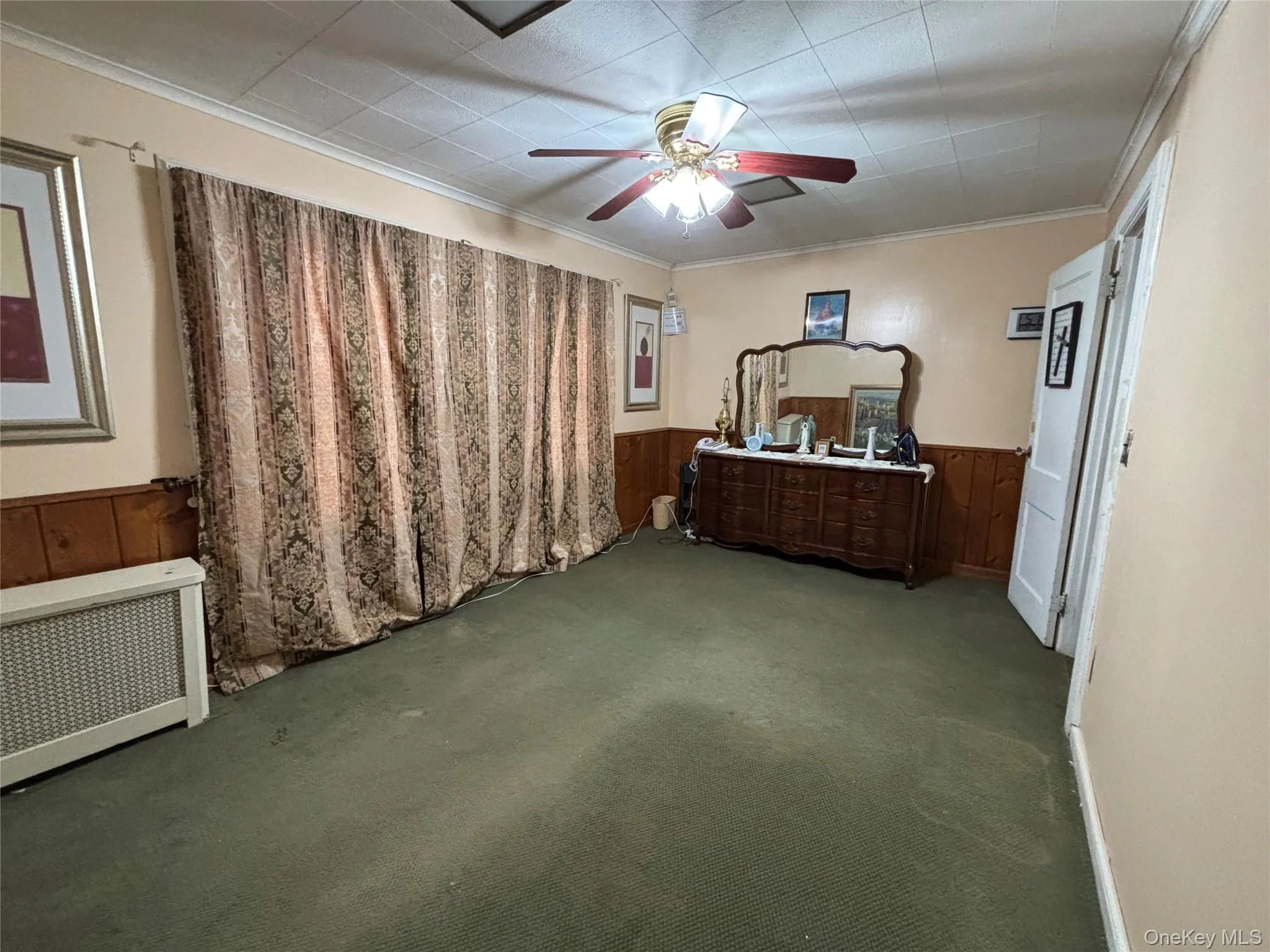 Bedroom with radiator heating unit, carpet, crown molding, wooden walls, and a ceiling fan Bedroom with radiator heating unit, carpet, crown molding, wooden walls, and a ceiling fan