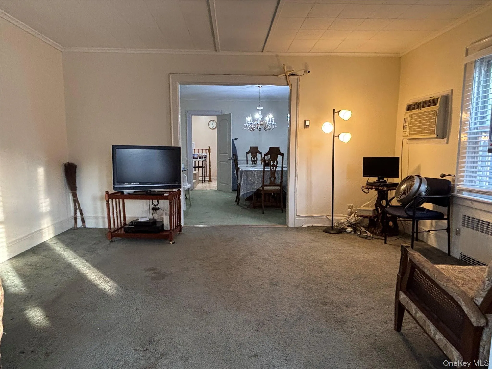 Carpeted living room featuring a chandelier, crown molding, radiator, and a wall unit AC Carpeted living room featuring a chandelier, crown molding, radiator, and a wall unit AC