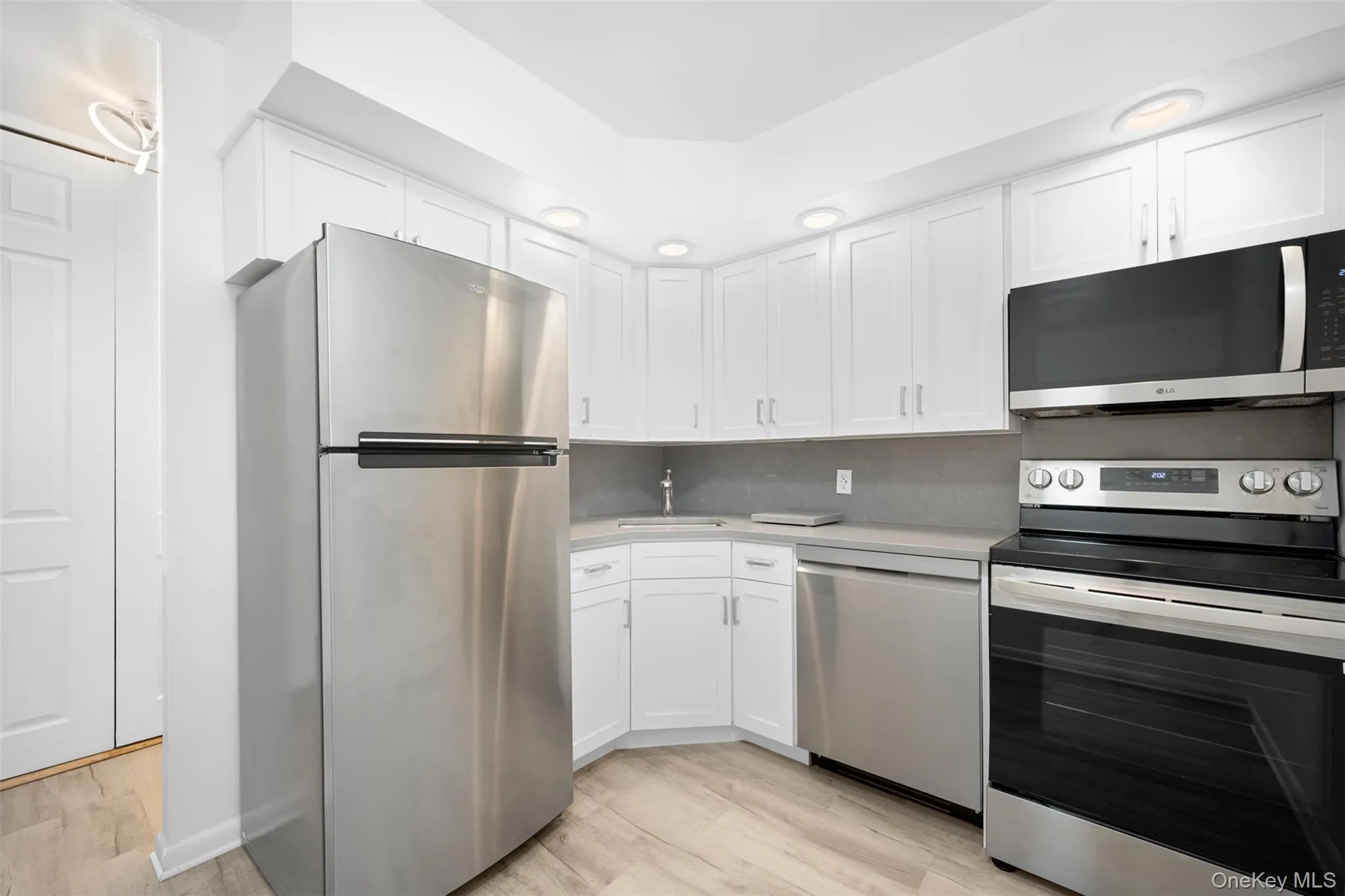 Kitchen featuring stainless steel appliances, light Stone countertops, white cabinetry, and light wood-style flooring Kitchen featuring stainless steel appliances, light Stone countertops, white cabinetry, and light wood-style flooring