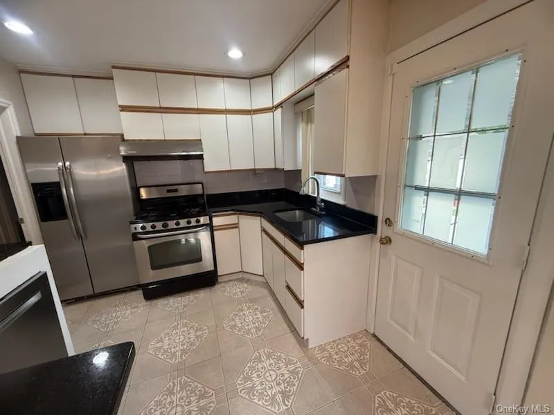 Kitchen featuring appliances with stainless steel finishes, backsplash, white cabinetry, light tile patterned floors, and under cabinet range hood Kitchen featuring appliances with stainless steel finishes, backsplash, white cabinetry, light tile patterned floors, and under cabinet range hood