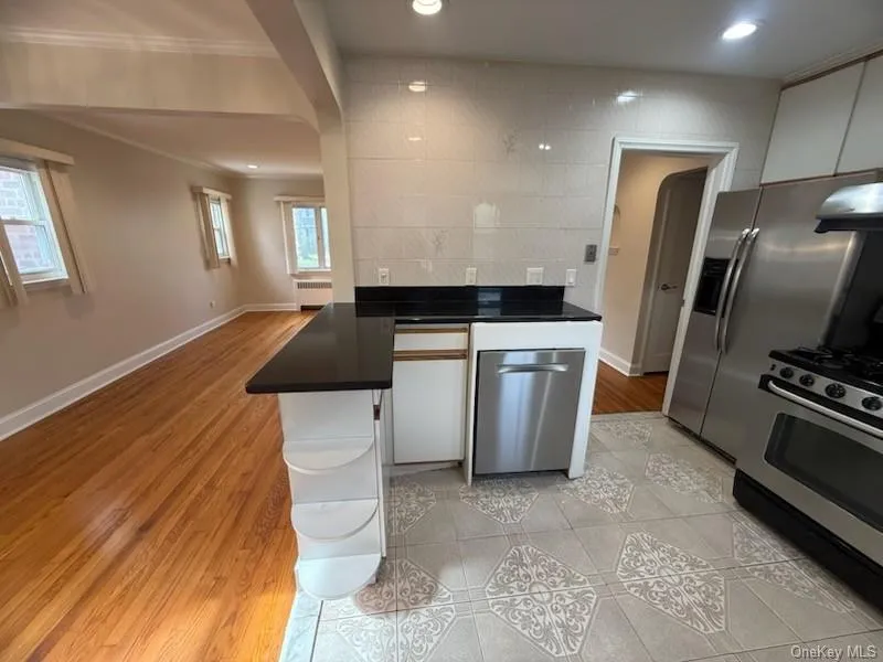 Kitchen with stainless steel appliances, light wood-style floors, white cabinets, ornamental molding, and a peninsula Kitchen with stainless steel appliances, light wood-style floors, white cabinets, ornamental molding, and a peninsula