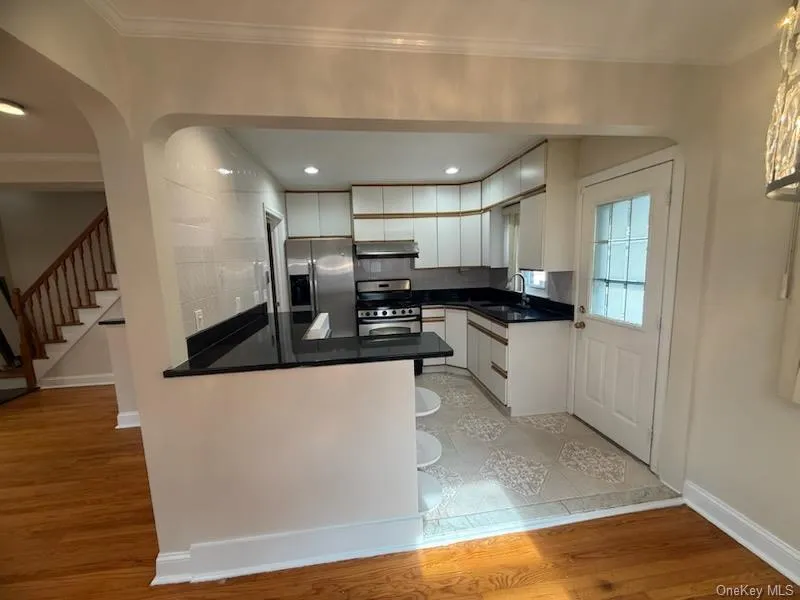 Kitchen featuring white cabinets, ornamental molding, stainless steel appliances, tasteful backsplash, and light wood-style floors Kitchen featuring white cabinets, ornamental molding, stainless steel appliances, tasteful backsplash, and light wood-style floors