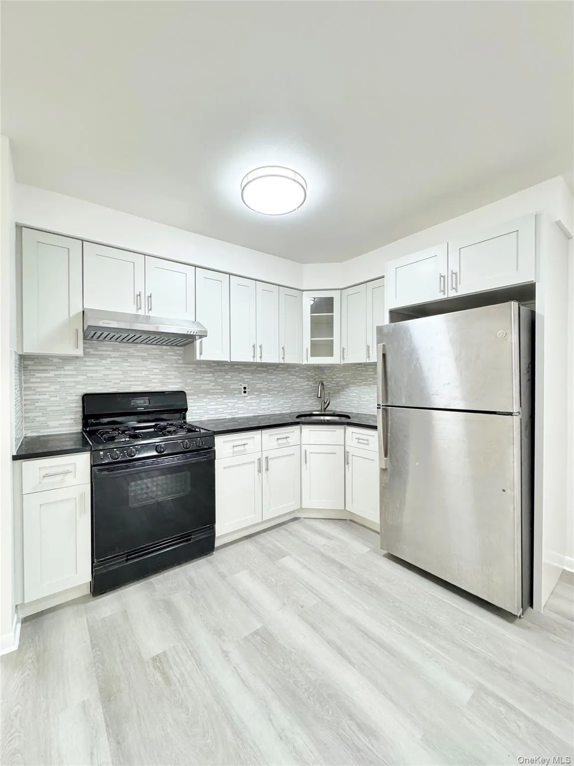 Kitchen featuring black range with gas stovetop, freestanding refrigerator, backsplash, and white cabinets Kitchen featuring black range with gas stovetop, freestanding refrigerator, backsplash, and white cabinets