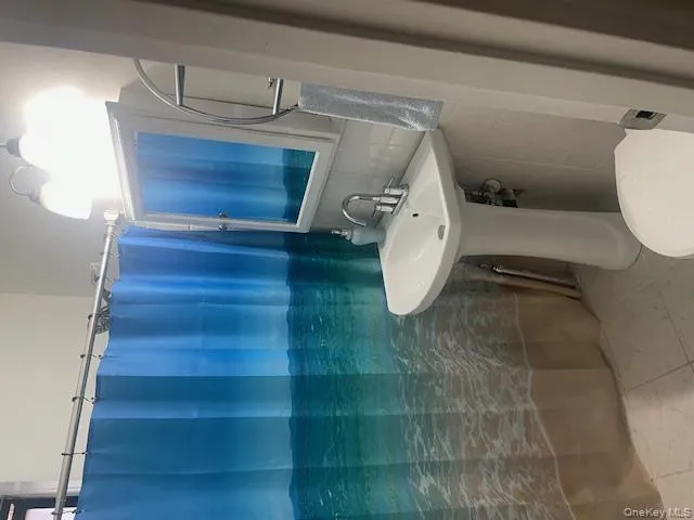 Bathroom featuring curtained shower, light tile patterned flooring, decorative backsplash, and tile walls Bathroom featuring curtained shower, light tile patterned flooring, decorative backsplash, and tile walls