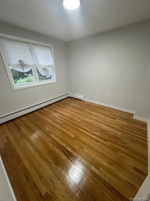 Unfurnished room with light wood-style flooring and a baseboard heating unit Unfurnished room with light wood-style flooring and a baseboard heating unit