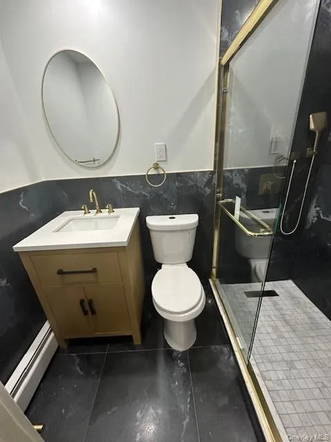 Bathroom featuring vanity, a stall shower, tile walls, wainscoting, and dark tile patterned floors Bathroom featuring vanity, a stall shower, tile walls, wainscoting, and dark tile patterned floors