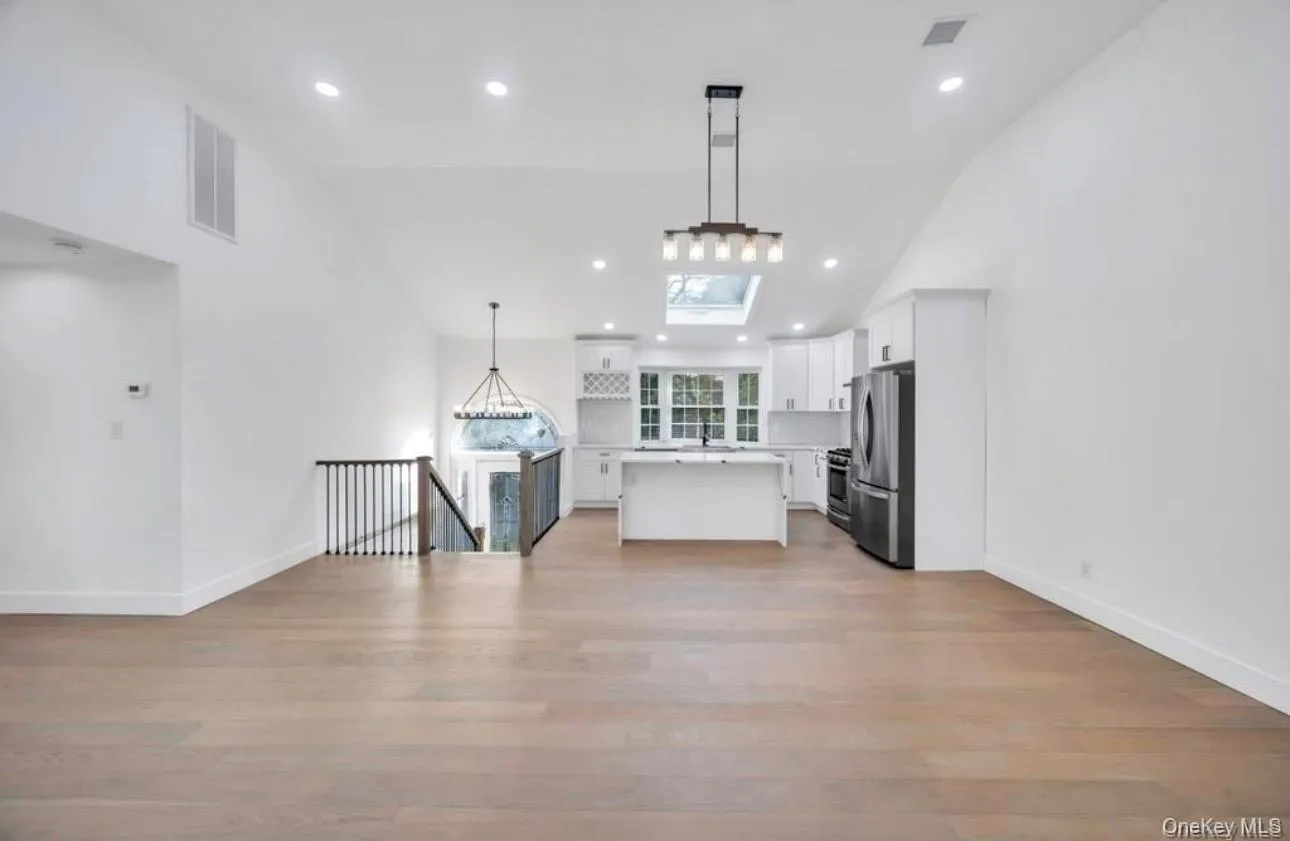 Kitchen with open floor plan, lofted ceiling, hanging light fixtures, white cabinets, and appliances with stainless steel finishes Kitchen with open floor plan, lofted ceiling, hanging light fixtures, white cabinets, and appliances with stainless steel finishes