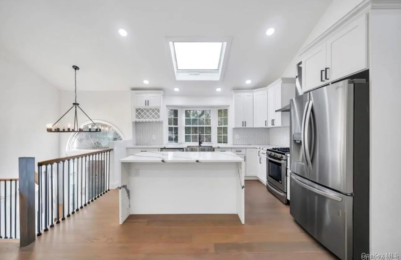 Kitchen featuring appliances with stainless steel finishes, a kitchen island, white cabinetry, light stone counters, and dark wood-style floors Kitchen featuring appliances with stainless steel finishes, a kitchen island, white cabinetry, light stone counters, and dark wood-style floors
