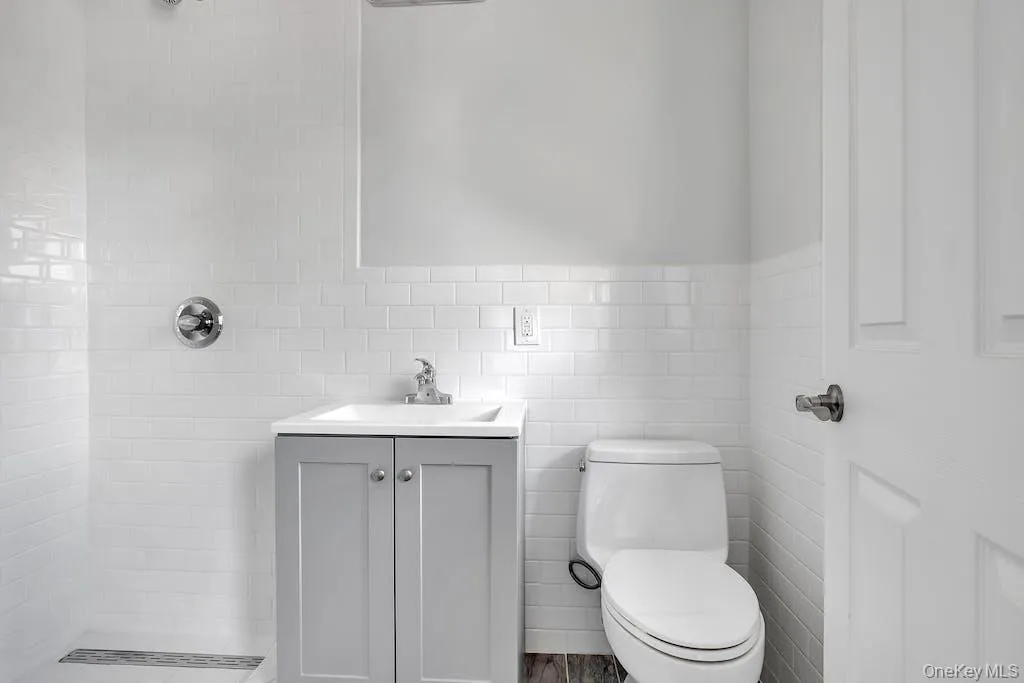 Full bath featuring tile walls, tiled shower, vanity, and a wainscoted wall Full bath featuring tile walls, tiled shower, vanity, and a wainscoted wall
